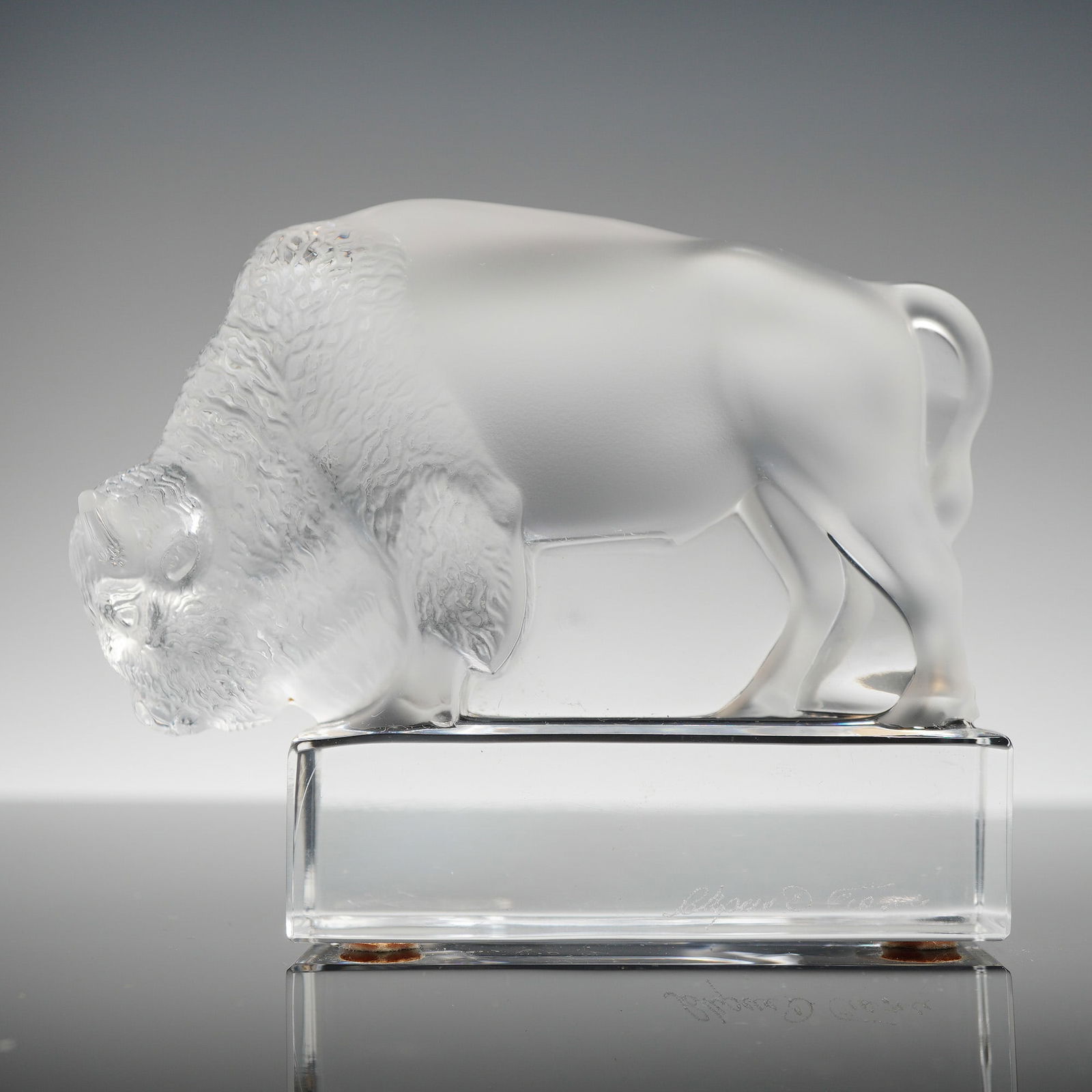 Lalique Frosted Crystal Figurine, Buffalo Bison: The piece is constructed from frosted and clear glass, featuring a textured mane and head that transitions into a smooth, frosted body. The animal is depicted in a standing, forward-leaning pose and i