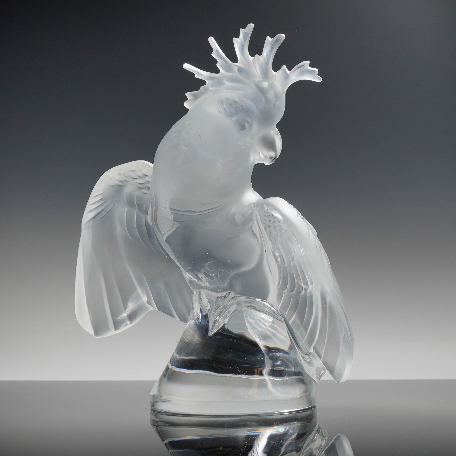 Lalique Crystal Ara Cockatoo Sculpture: The cockatoo is modeled with its wings partially spread and its characteristic crest raised. The piece features a combination of satin-finished frosted crystal for the body and plumage, set upon a pol