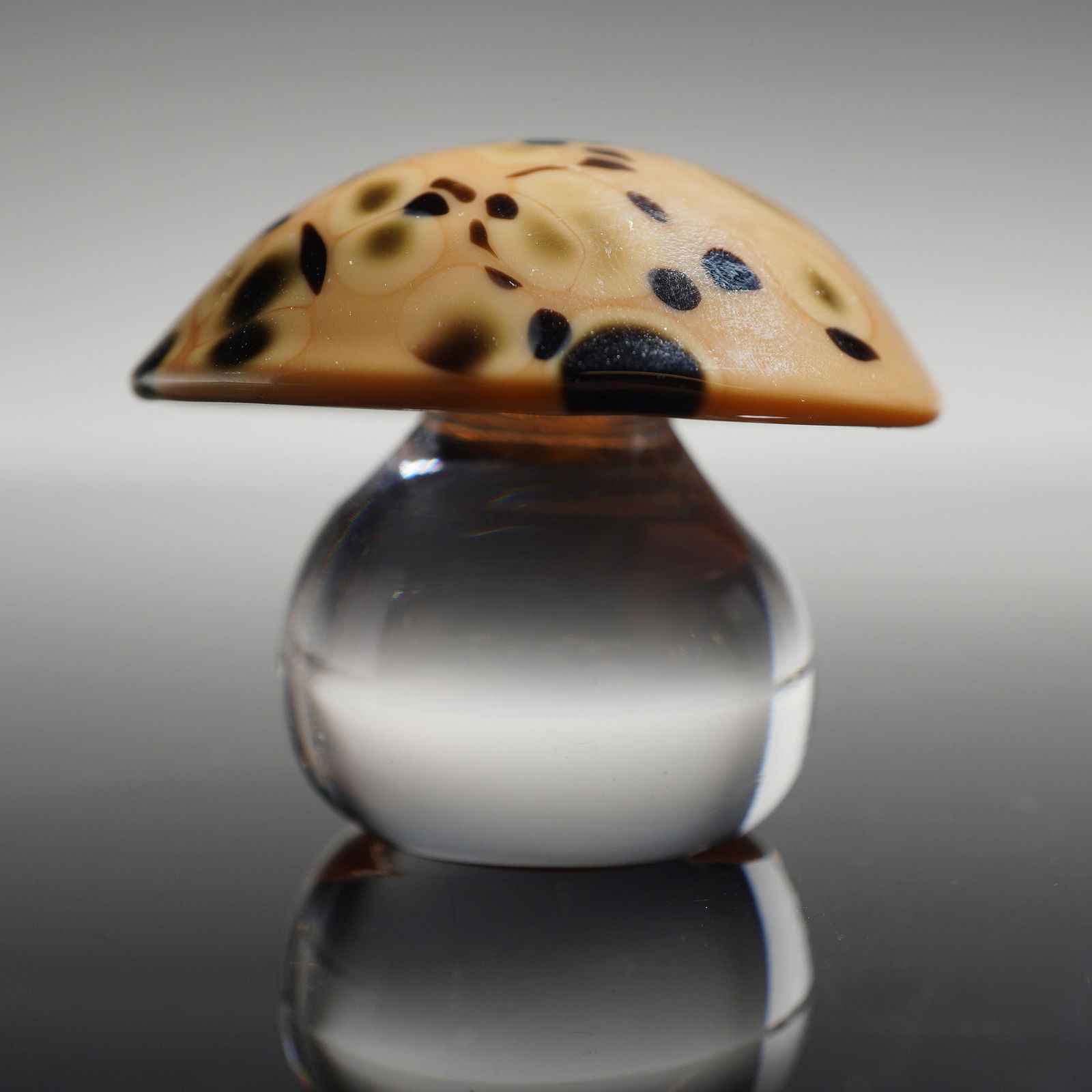 Orrefors Art Glass Mushroom Figurine: The object features a domed cap decorated with mottled beige and dark brown to black spotting. The cap is joined to a solid, bulbous stem of clear glass. The underside of the base is hand-etched with