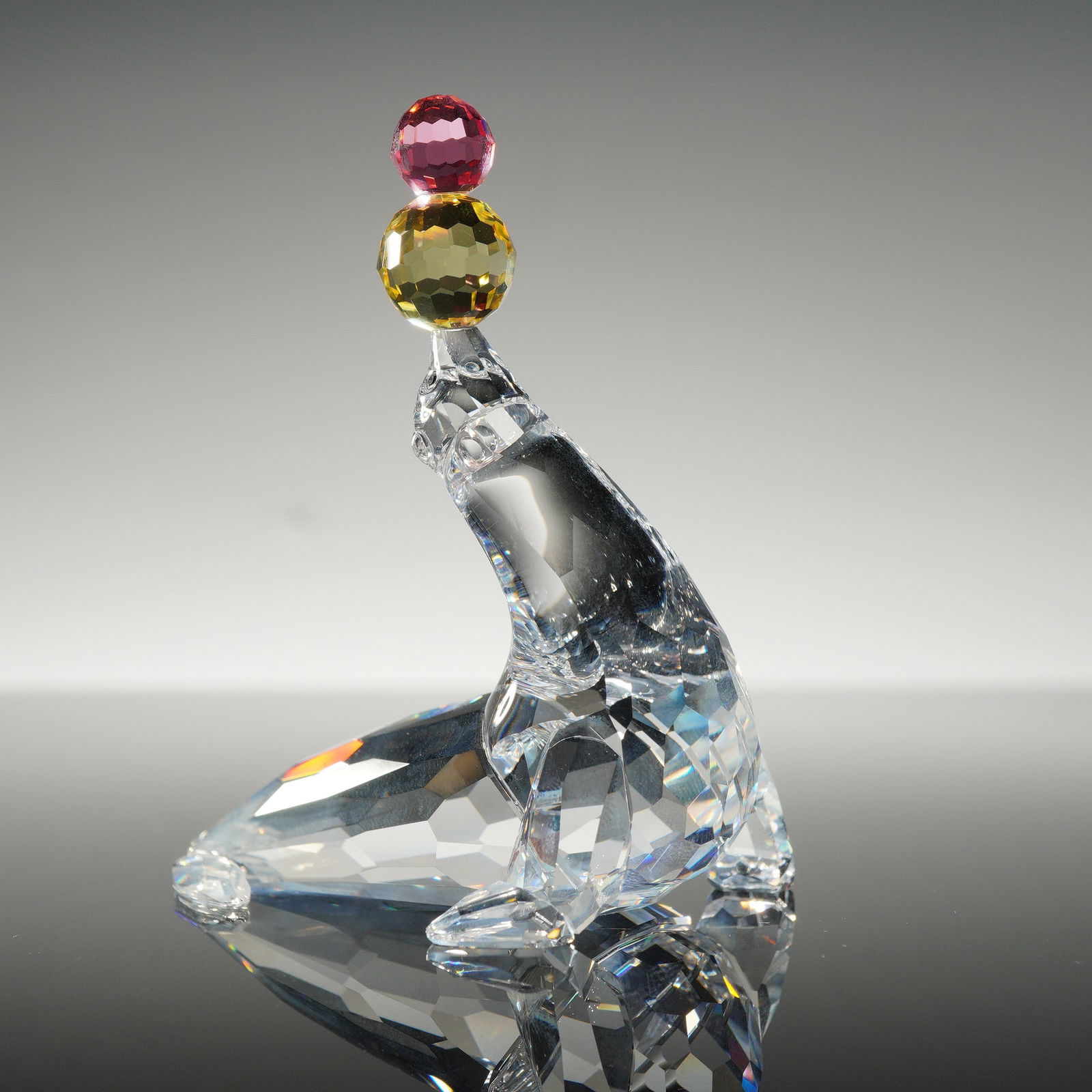 Swarovski Crystal Playing Seal With Balls Figurine: This Swarovski crystal figurine, identified as the Playing Seal with balls, model number 622526, is crafted from faceted lead crystal. The figure depicts a seal balancing two stacked, faceted spheres