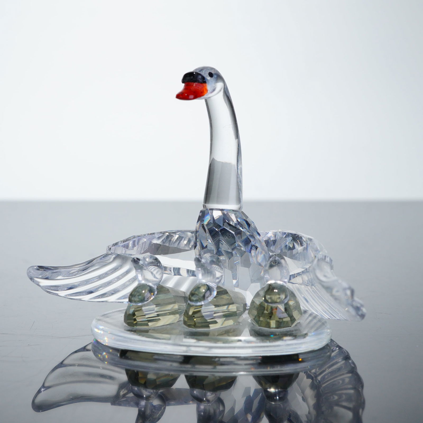Swarovski Silver Crystal Figurine, Swan Family: A Swarovski figurine from the Beauties of the Lake series. The composition features a central mother swan with outstretched wings sheltering three cygnets, all mounted on a smooth oval clear crystal b