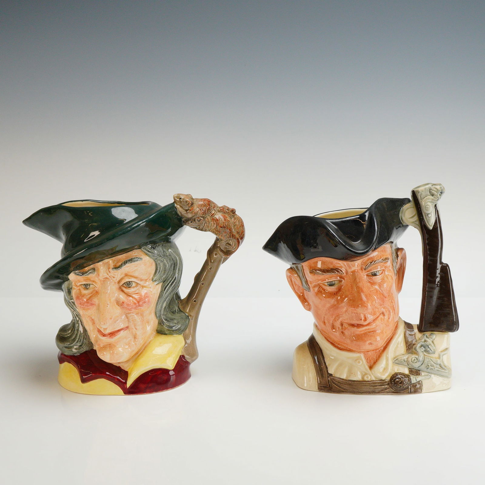 2pc Royal Doulton Character Jugs, Pied Piper and Gunsmith: This lot consists of two Royal Doulton hand-painted glazed ceramic character jugs. The first jug is titled Pied Piper, model number D6403, with a copyright date of 1953. It depicts the figure in a gre