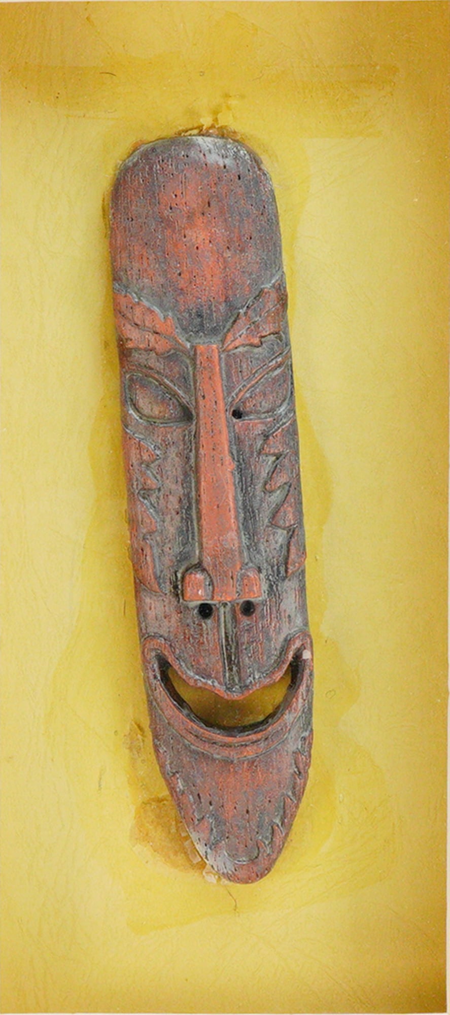 Framed Wooden Carving of a Tiki Face: This lot features a framed wooden carving of a tiki face. The elongated mask is hand-carved from wood and finished with a reddish-brown pigment, featuring stylized facial features and a prominent smil