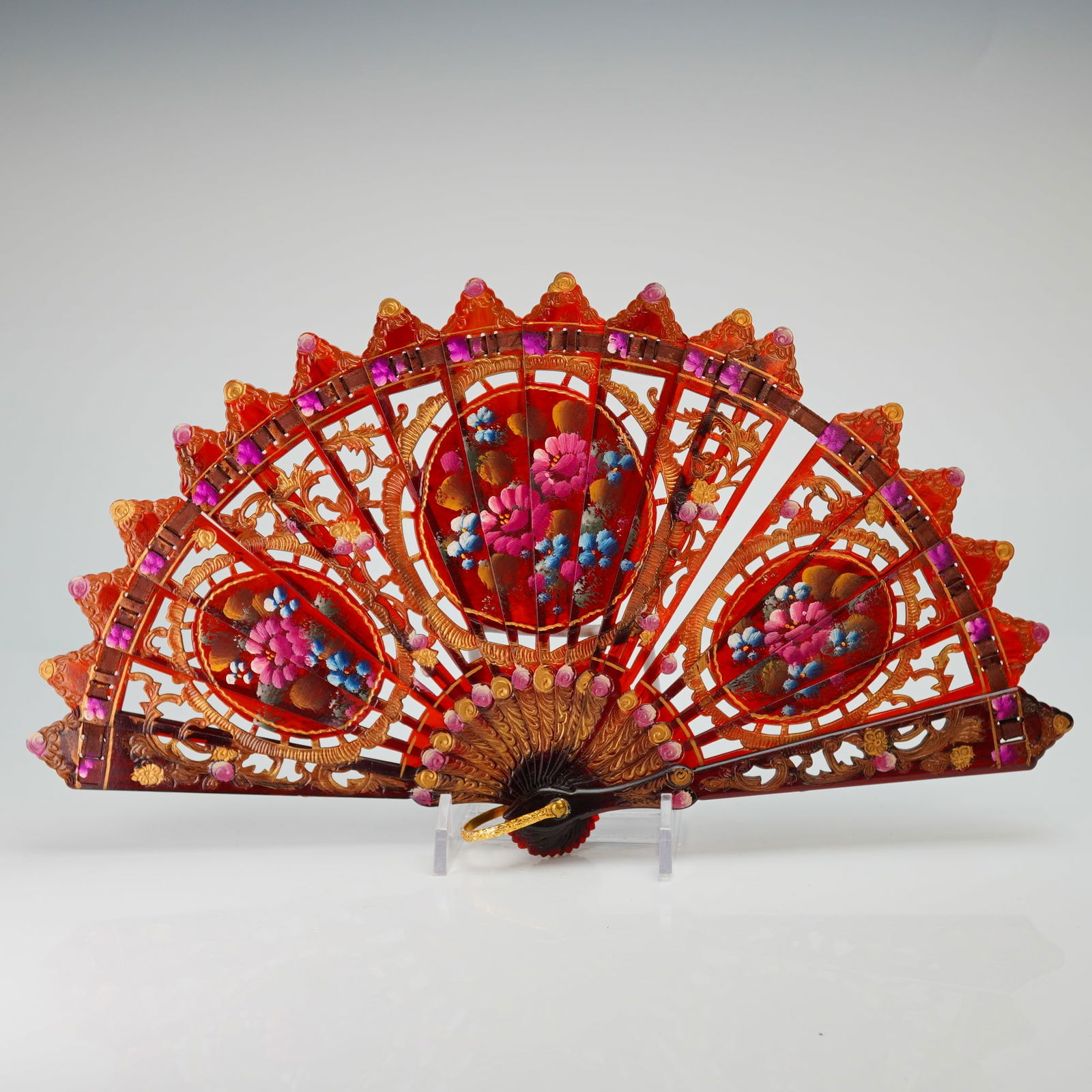 Spanish Hand Painted Floral Folding Fan: This Spanish folding fan, also known as an abanico, is crafted from a translucent amber-toned plastic material designed to imitate tortoiseshell. The brise-style construction features individual stick
