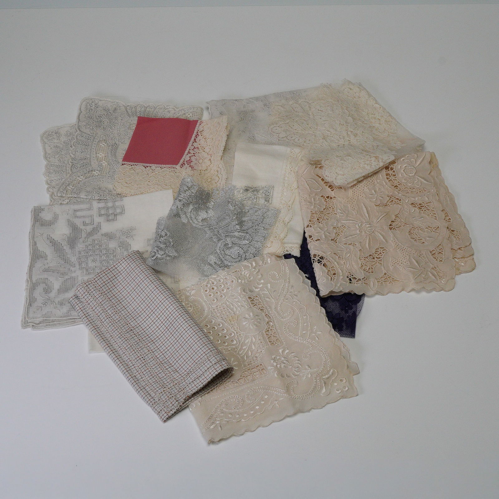 A Collection of Late 19th/Early 20th Century Embroidered Linens and Lace: A collection of various textile pieces, predominantly featuring different types of lace and embroidered fabrics. The group includes a rectangular white linen textile showcasing intricate white work em