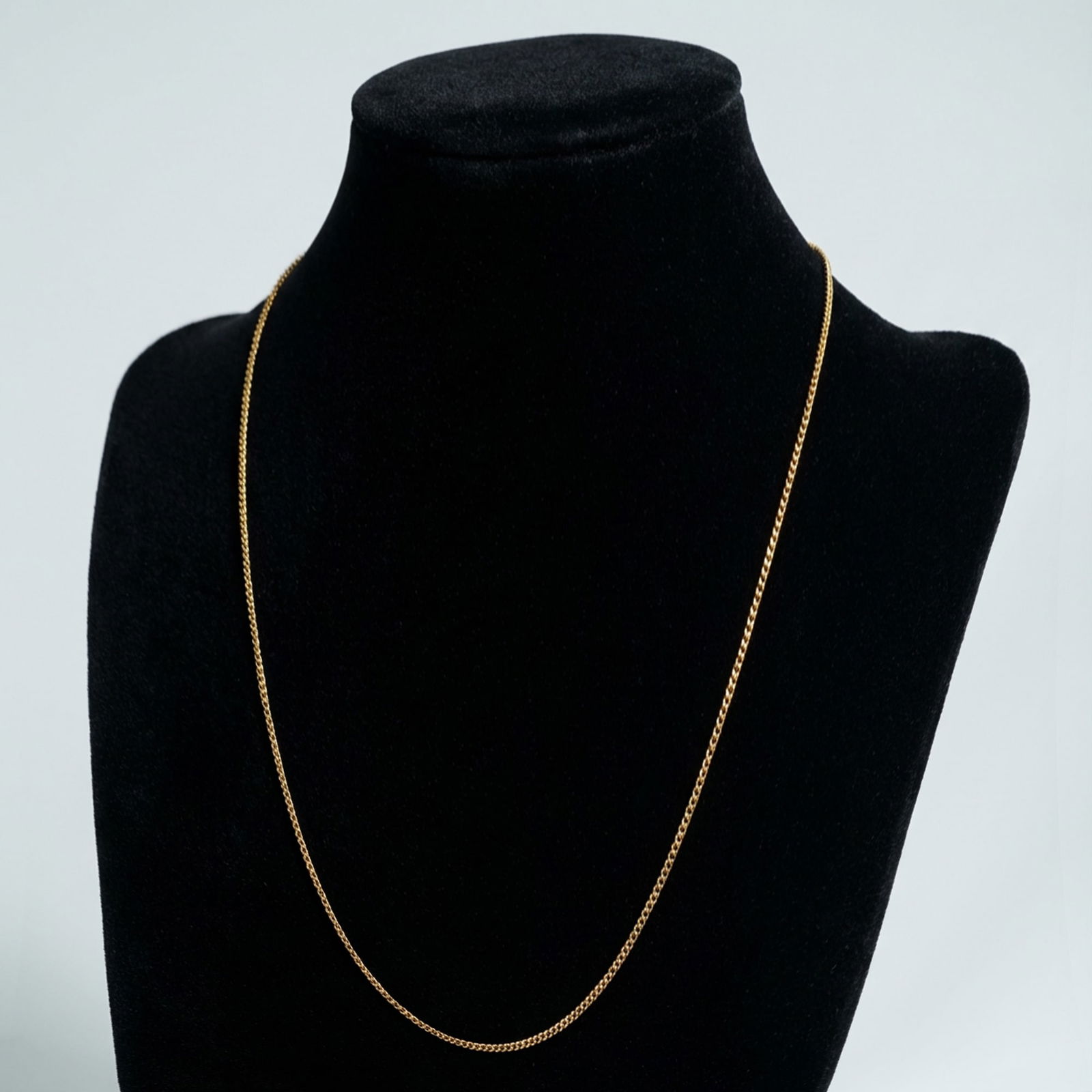 Gold-Plated Narrow Curb Link Chain Necklace: A gold-plated chain necklace that features a tightly woven, narrow curb link design (flattened wheat or foxtail style.) The necklace is secured by a functional spring ring clasp mechanism. Stamped wit