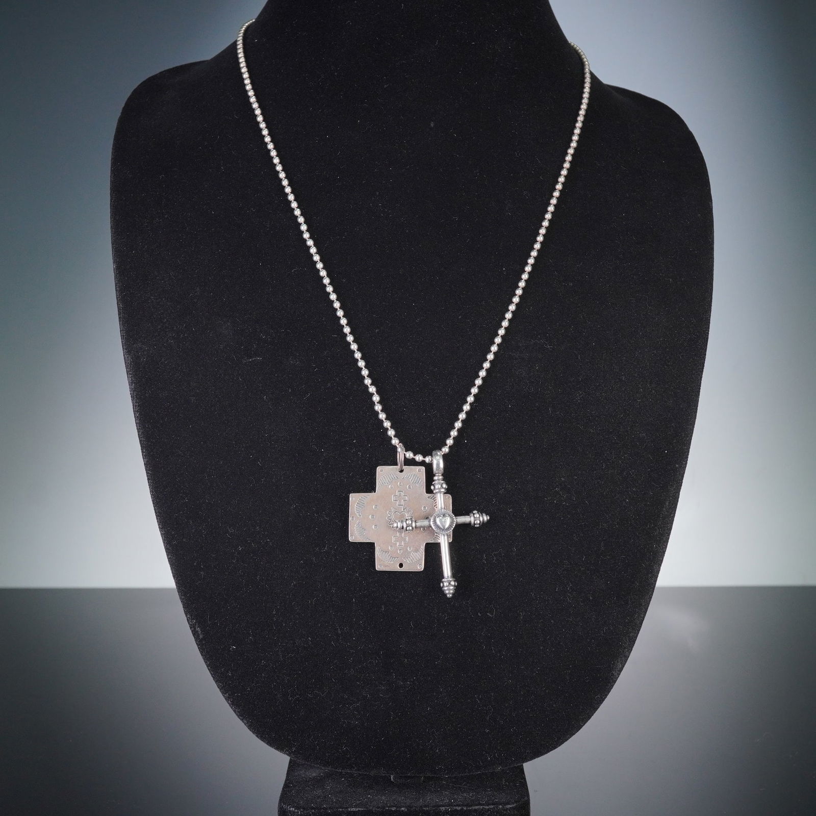 Sterling Silver Double Cross Pendant Necklace: A sterling silver necklace featuring a ball chain suspending a double pendant composed of two distinct cross designs. One pendant is a flat, stamped cross adorned with geometric patterns, smaller cros