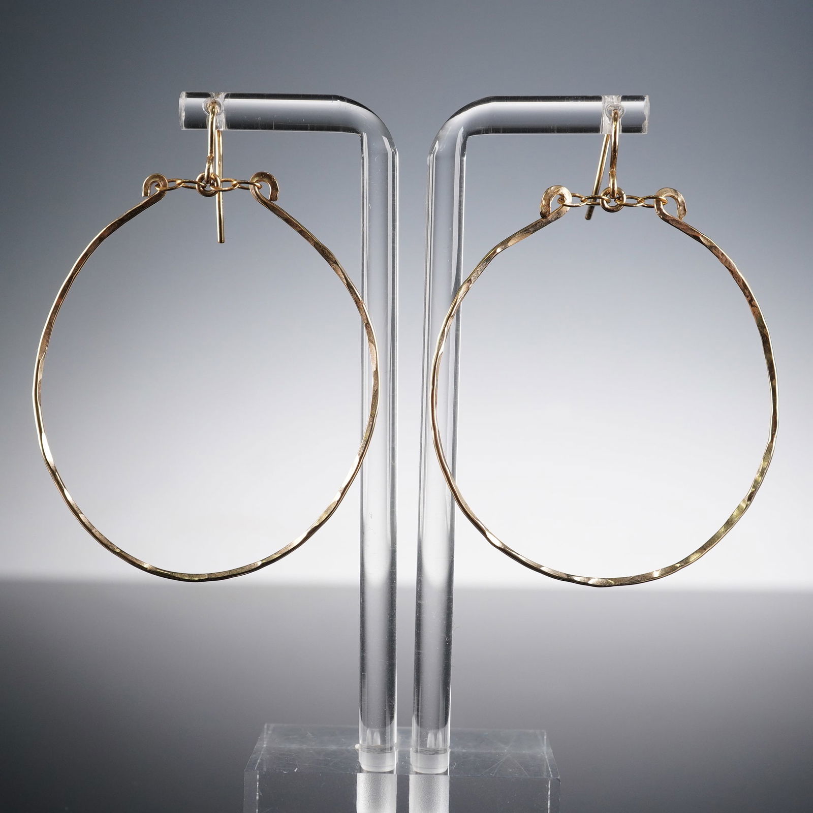 A Pair of 14K GF Hoop Earrings: This lot comprises a pair of large, circular hoop earrings exhibiting a distinctive textured finish. Each earring features a simple fish hook-style ear wire, connected to the main hoop via small jump