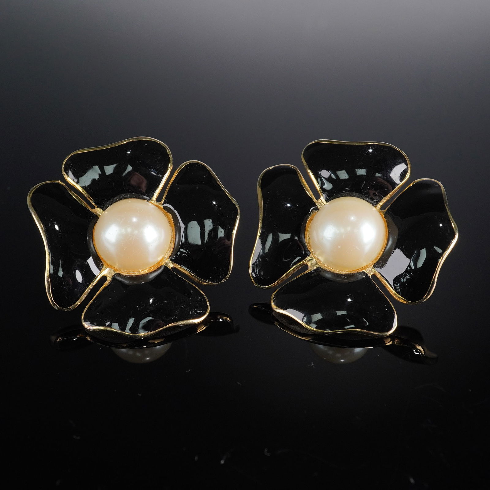 Valentino Gold-Tone Black Enamel Faux Pearl Floral Earrings: A pair of Valentino gold-tone, black enamel, and faux pearl floral clip-on earrings. Each earring features a five-petal floral design with glossy black enamel petals, centered around a cream-colored f