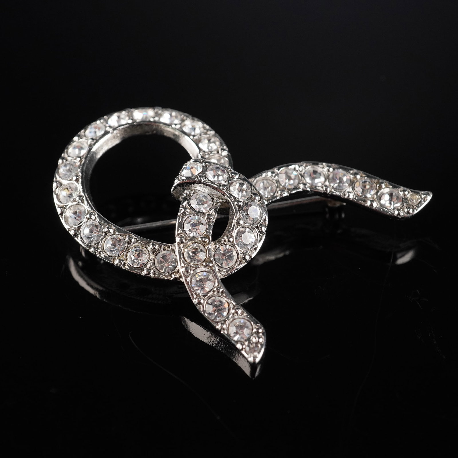 Sonia Rykiel Silver-Tone Rhinestone Knot Brooch: A Sonia Rykiel silver-tone rhinestone knot brooch designed with a stylized ribbon featuring an intertwined circular element. The entire front surface is pave-set with numerous round, faceted clear rhi