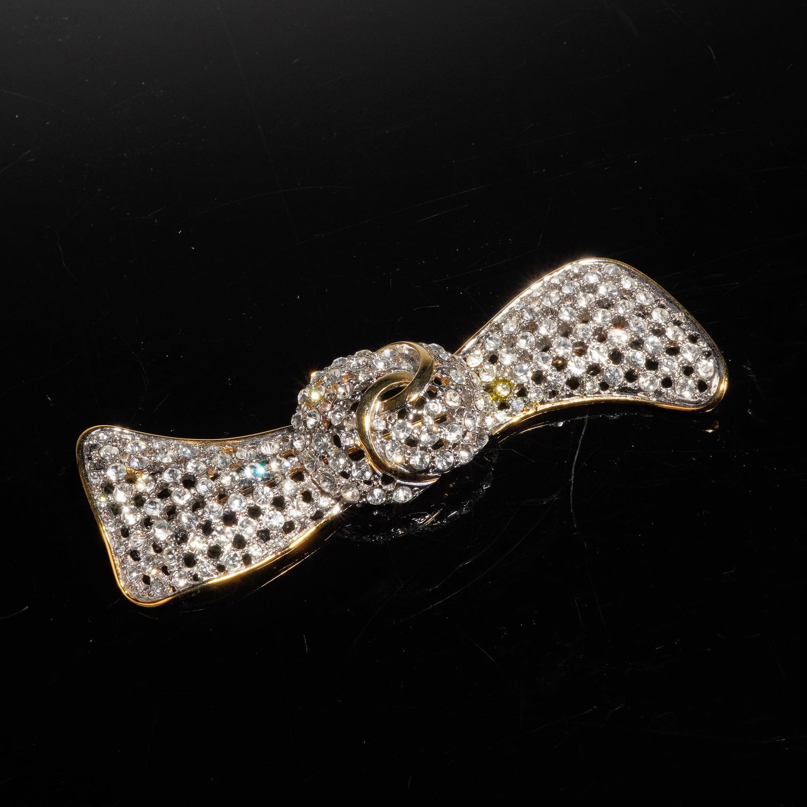 Valentino Night Gold Toned Rhinestone Bow Brooch: A vintage Valentino Gold-toned and rhinestone bow brooch, attributed to the Valentino Night diffusion line. The piece is constructed of gold-toned base metal stylized in the form of a knotted bow with