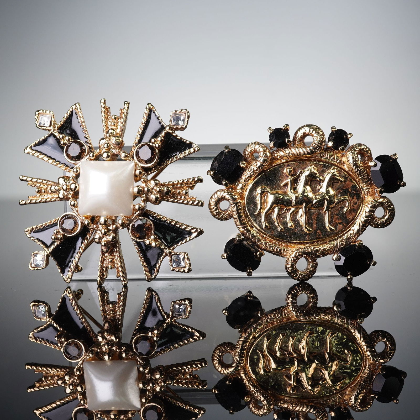 2pc St Johns Gold-Tone Brooches: Two St Johns gold-tone metal brooches, each equipped with a standard pin back. The first brooch features a radiating, Maltese cross-like design centered by a white cabochon, surrounded by alternating