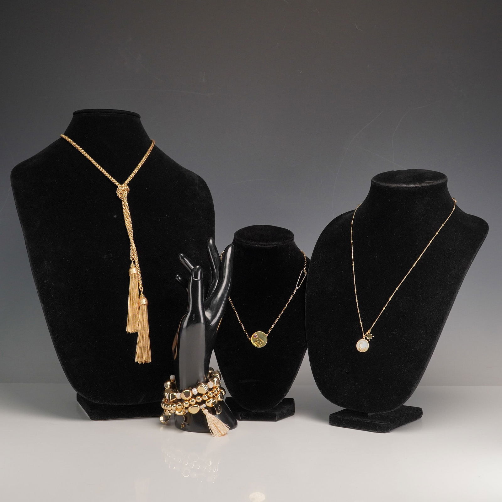 A Collection of Four Contemporary Gold-Tone Costume Jewelry Pieces: A collection of four contemporary costume jewelry pieces, crafted primarily from a polished gold-tone metal. The lot comprises a long lariat-style necklace with two tassel ends, a delicate chain