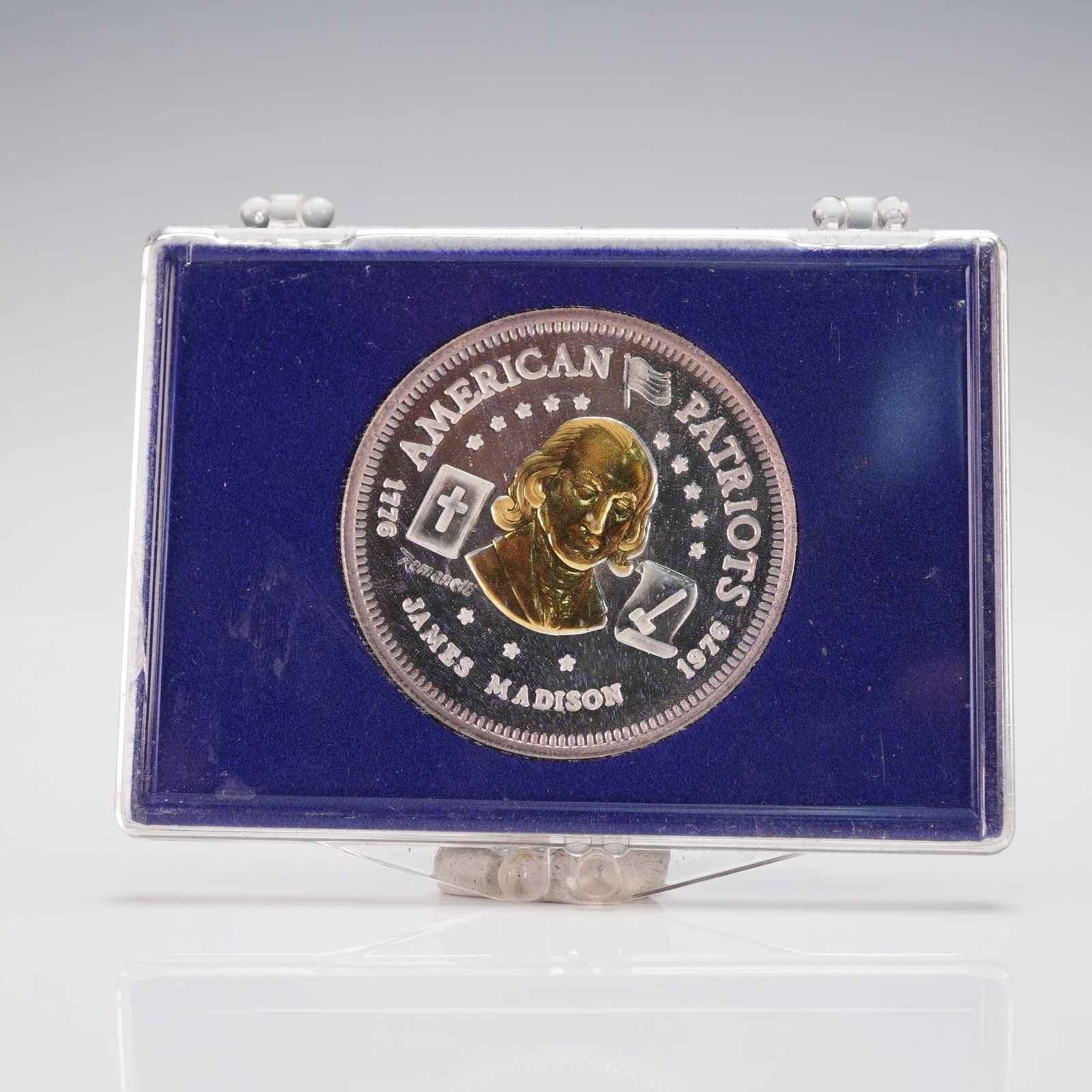 1976-L James Madison American Patriots Silver and Gold Bullion: An obverse portrait of James Madison surrounded by stars, crossed flags, and the inscriptions AMERICAN PATRIOTS, 1776, 1976, and JAMES MADISON. The reverse displays a laurel wreath encircling the