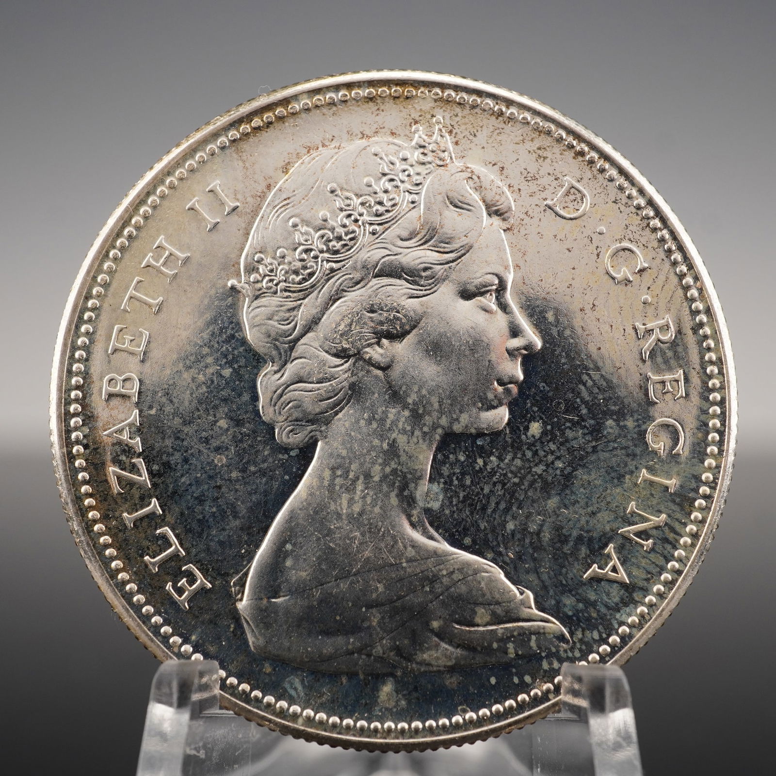 1967 Canadian Elizabeth II One Dollar Coin: Commemorative issue marking the 100th anniversary of the Confederation of Canada. Struck in .800 fine silver (80% silver, 20% copper). The obverse features the right-facing bust of Queen Elizabeth II