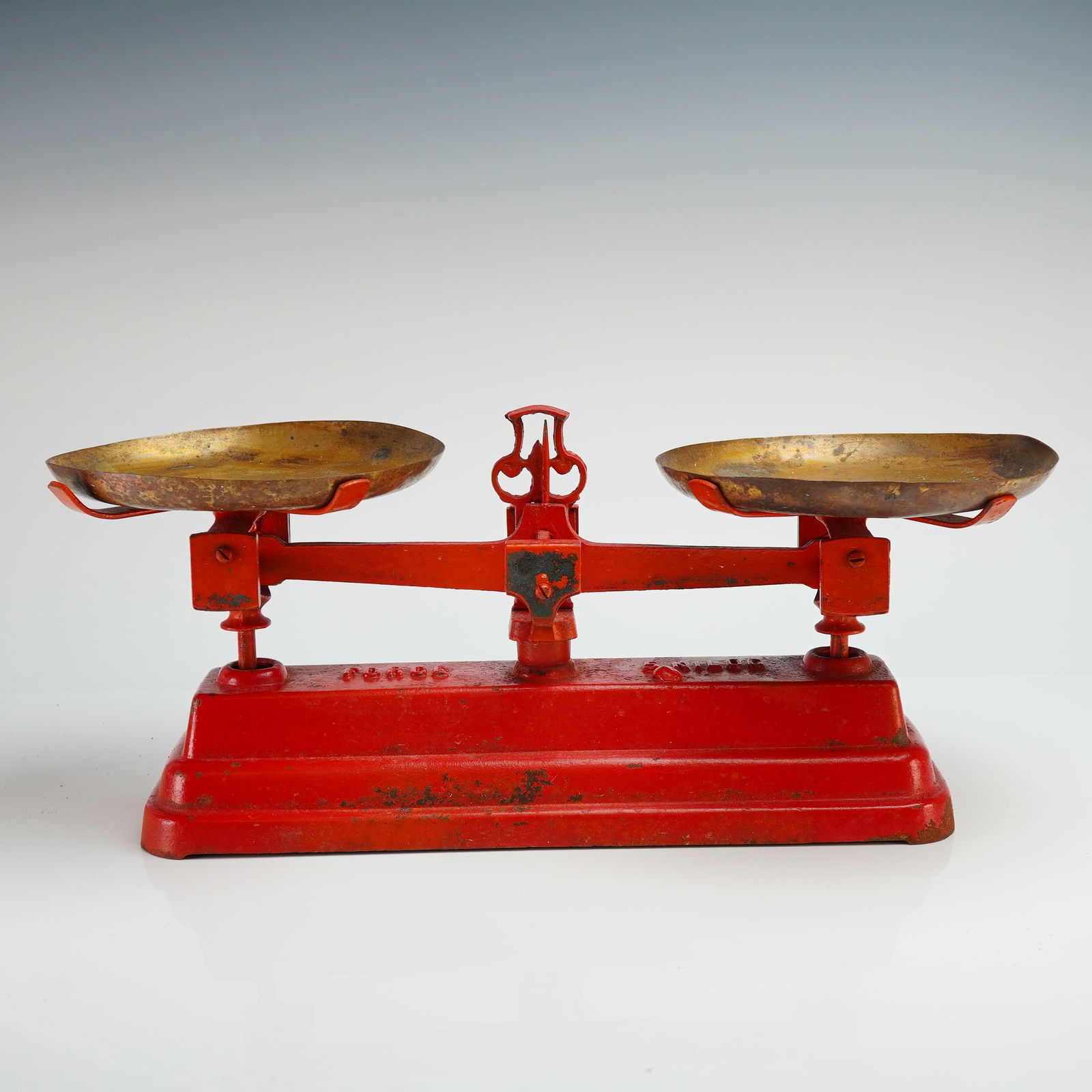 Force Cast Iron Balance Scale with Brass Pans: This mechanical balance scale is constructed with a cast iron base and balance arm finished in a weathered red paint. These cast iron scales with brass pans feature two circular, shallow weighing