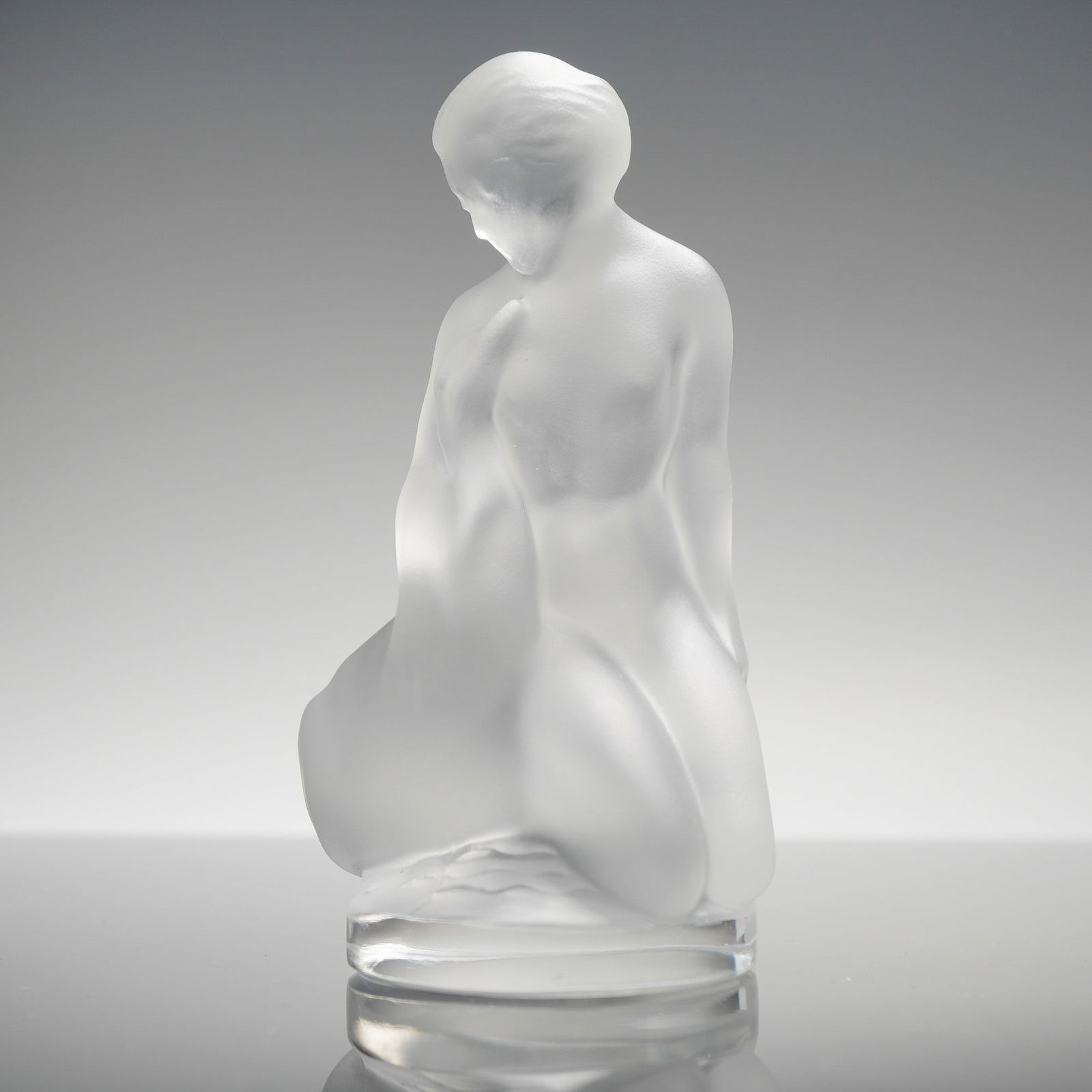 Lalique Frosted Crystal Figurine, Leda and the Swan: The sculpture depicts a kneeling female nude in a contemplative pose. The piece is constructed from satin-finished translucent crystal, which contrasts with the polished clear finish of the integral c