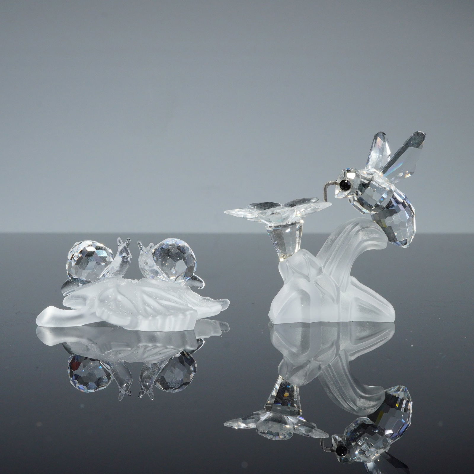 2pc Swarovski Silver Crystal Figurines, Bee and Snails on Leaf: A pair of Swarovski Silver Crystal figurines crafted from faceted and frosted lead crystal. The collection includes a bumble bee figurine, identified as model 166185, featuring a faceted body and blac
