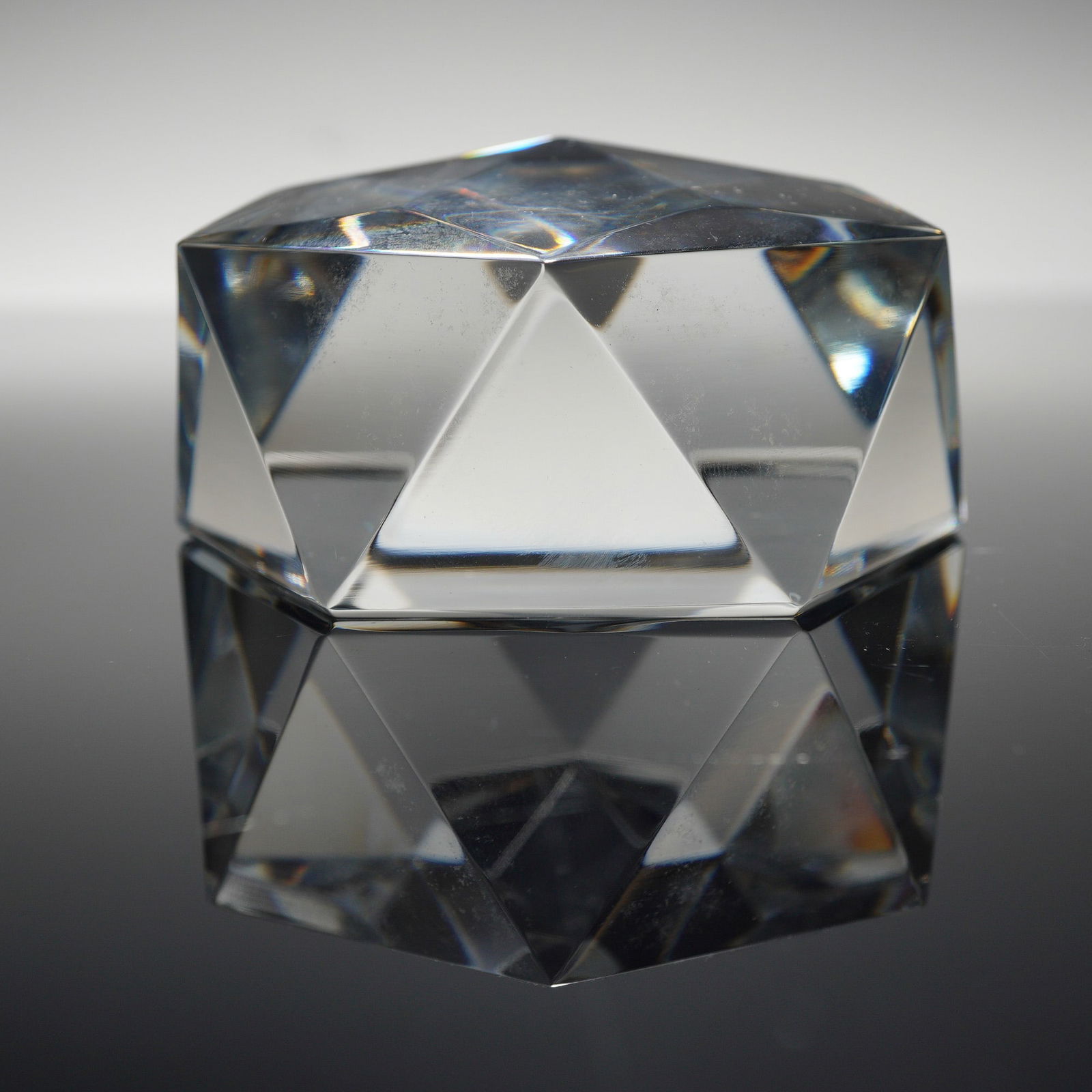 Baccarat Crystal Prism Geometric Paperweight: The object is crafted from clear crystal in a multifaceted polyhedral form featuring several sharp planes designed for light refraction. The base of the piece displays the authentic acid-etched circul