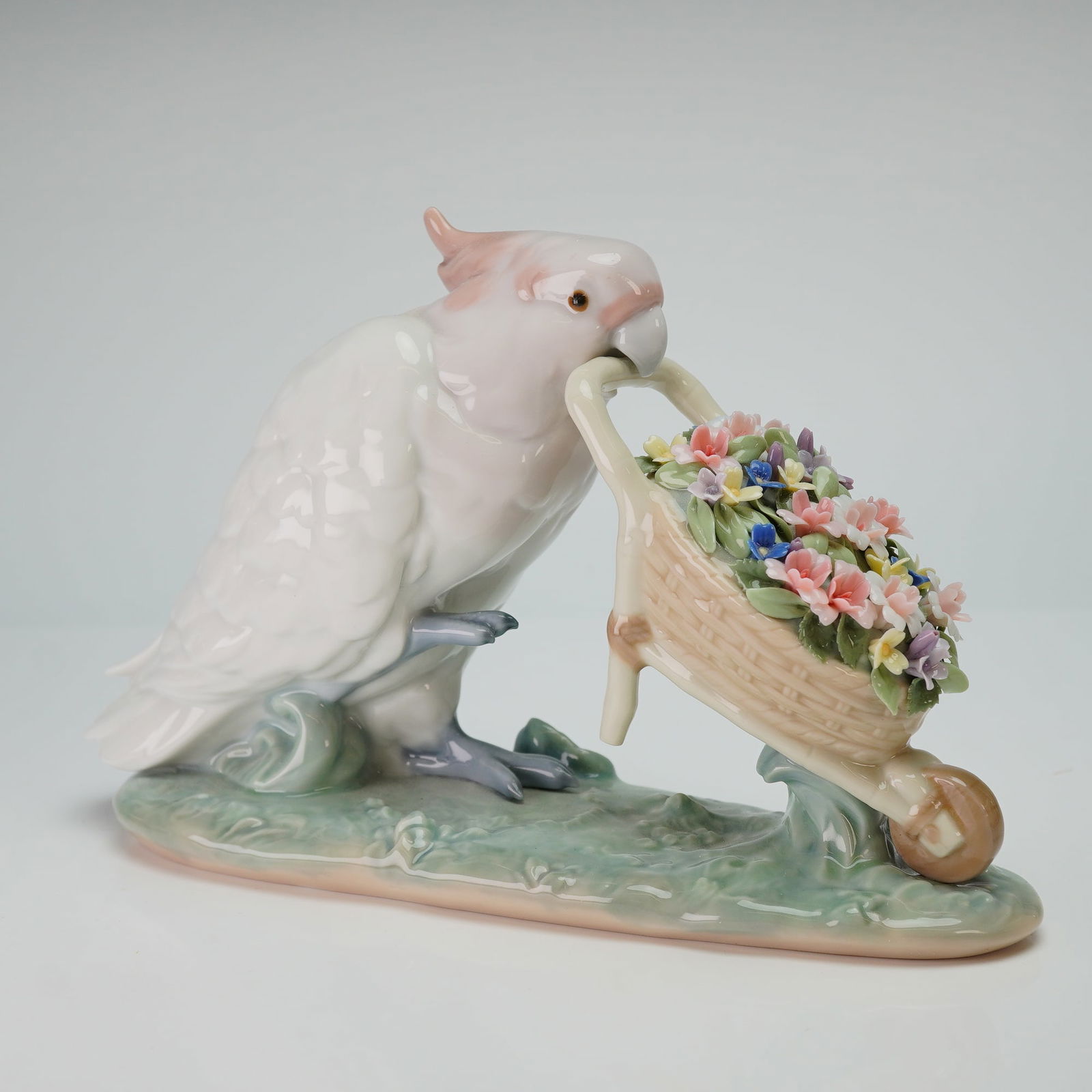 Lladro Figurine, How Skillful 1006517: This Lladro glazed porcelain figurine, titled How Skillful! and identified as item 1006517, depicts a white cockatoo with a pale pink crest. The bird is modeled holding a basket-style wheelbarrow in i