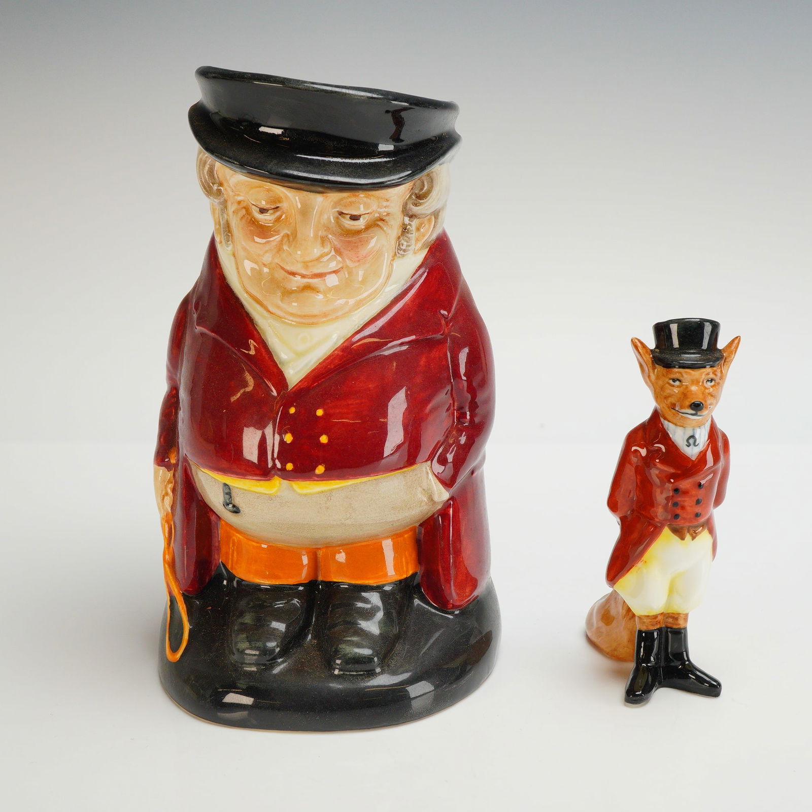 2pc Royal Doulton Bone China Pieces, The Huntsman Jug and Fox Figurine: Two Royal Doulton glazed ceramic pieces featuring traditional English hunting motifs. The collection includes a large character jug titled The Huntsman, model D6320, and an anthropomorphic fox figurin