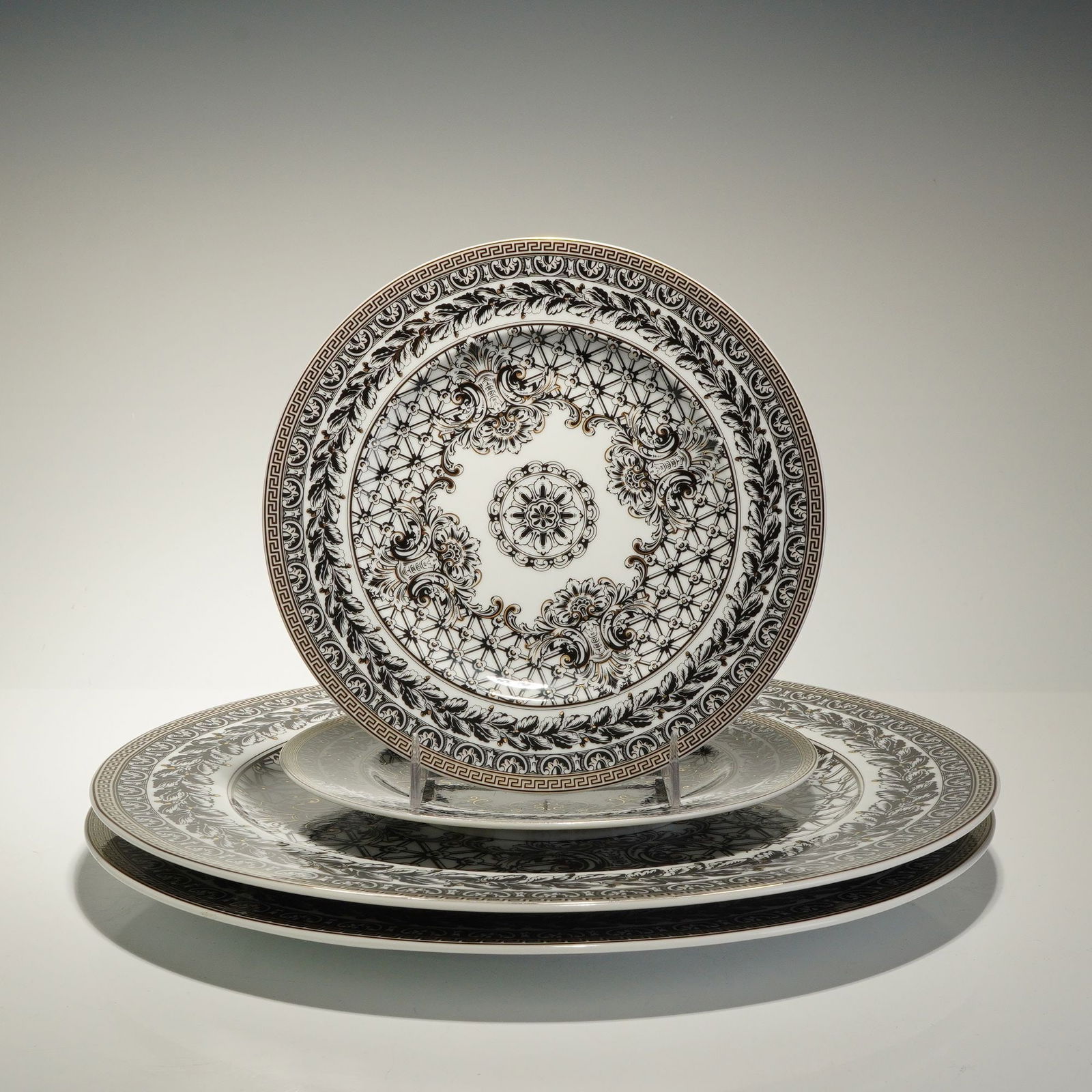 4pc Set of Rosenthal Versace Porcelain Plates, Marqueterie: These pieces feature black and white transfer-printed designs of scrolling acanthus leaves, floral medallions, and a geometric lattice background. Each plate is accented with gold gilt and finished wi