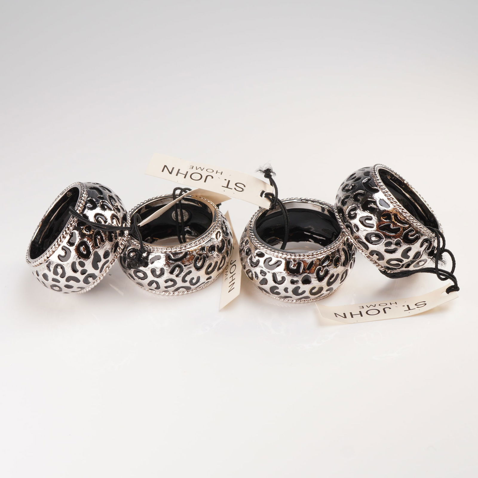 Set of 4 St. John Home Cheetah Print Napkin Rings: A set of four contemporary napkin rings manufactured by St. John Home, featuring the stylized Cheetah Print (also referred to as Panther pattern). Each cylindrical ring is constructed of silver-tone m