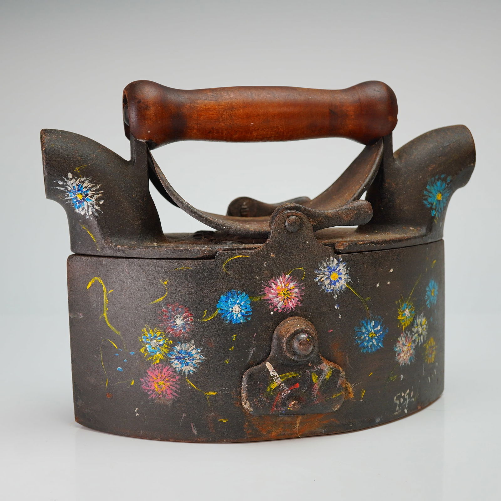 Folk Art Painte Cast Iron Charcoal Sad Iron: This antique cast iron charcoal sad iron features a heavy, dark-toned metal body with a wooden handle and two flared chimneys. The exterior is embellished with hand-painted folk art floral motifs in