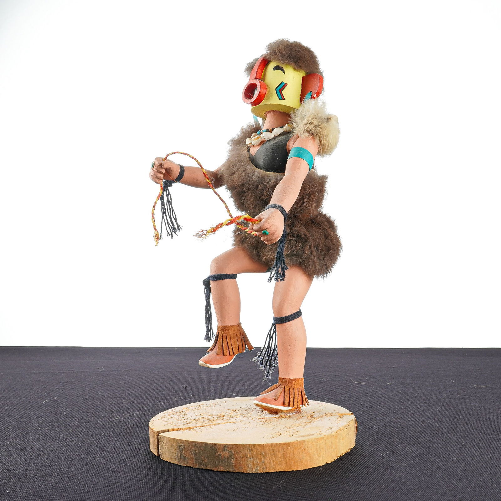 Native American Kachina Doll, Heheya Kachina: This hand-carved Hopi Heheya wooden kachina doll is depicted in a dynamic dancing pose and mounted on a natural circular wood slice base. The figure represents a man in fur holding a rope and wearing