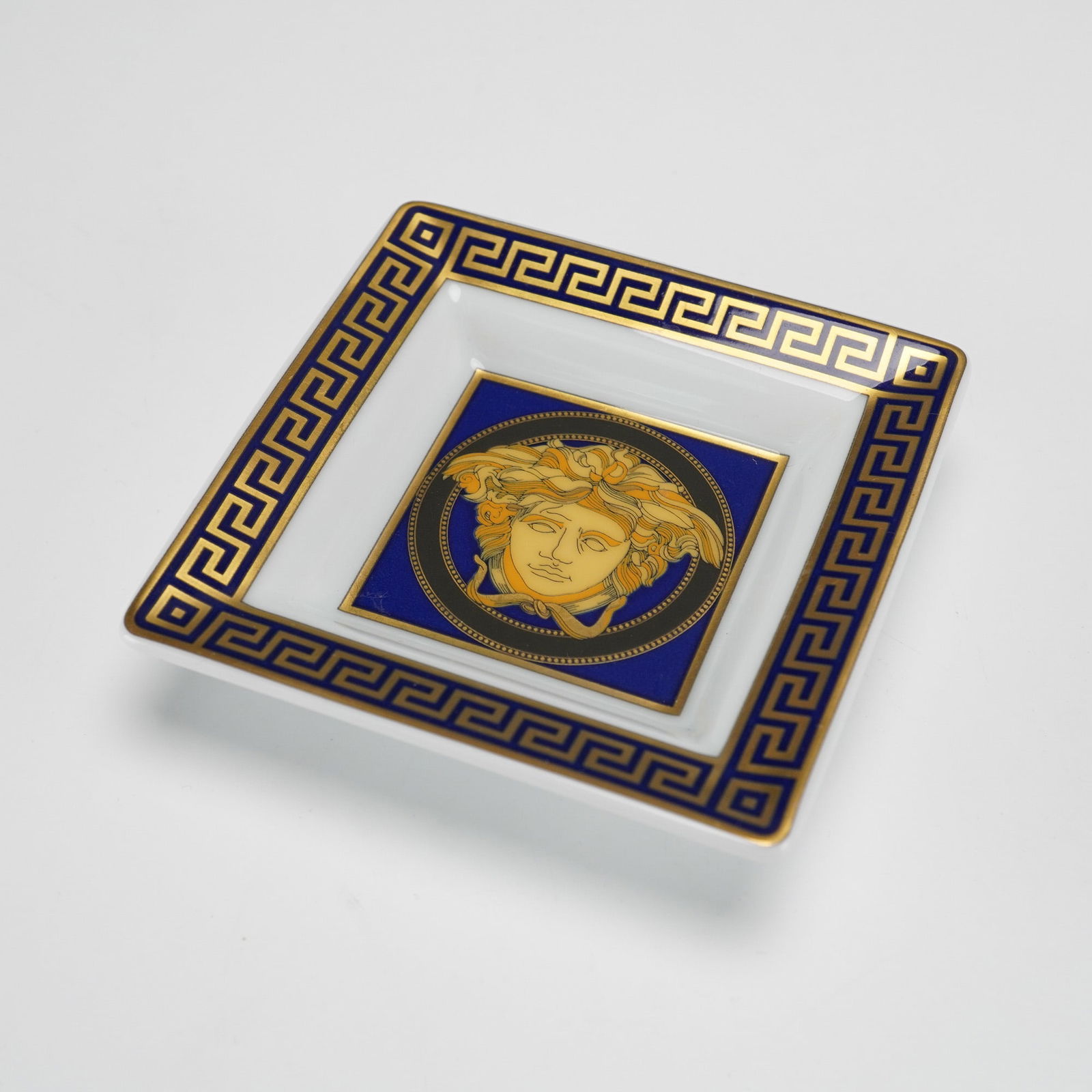 Versace Rosenthal Medusa Blue Porcelain Trinket Dish: A Versace Rosenthal 'Medusa Blue' square trinket porcelain dish that features a glossy white ground bordered by a gold and cobalt blue Greek key (Meander) pattern, encircling a central circular motif