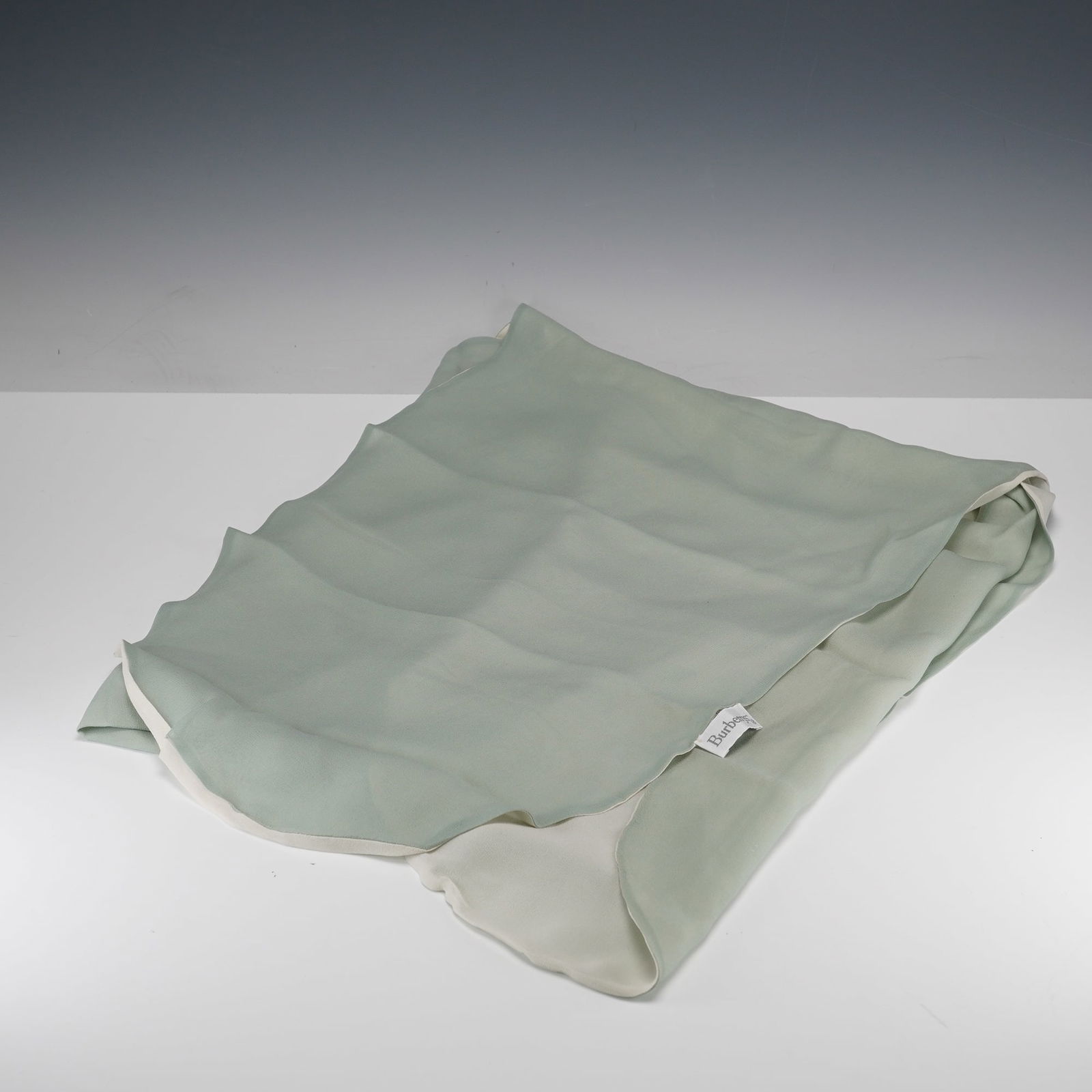 A Burberrys Reversible Sage Green and Cream Silk Scarf: A vintage Burberrys reversible silk scarf. The item features a two-tone design, with one side in a light sage green and the other in an off-white or cream hue. It is crafted from a fine, lightweight