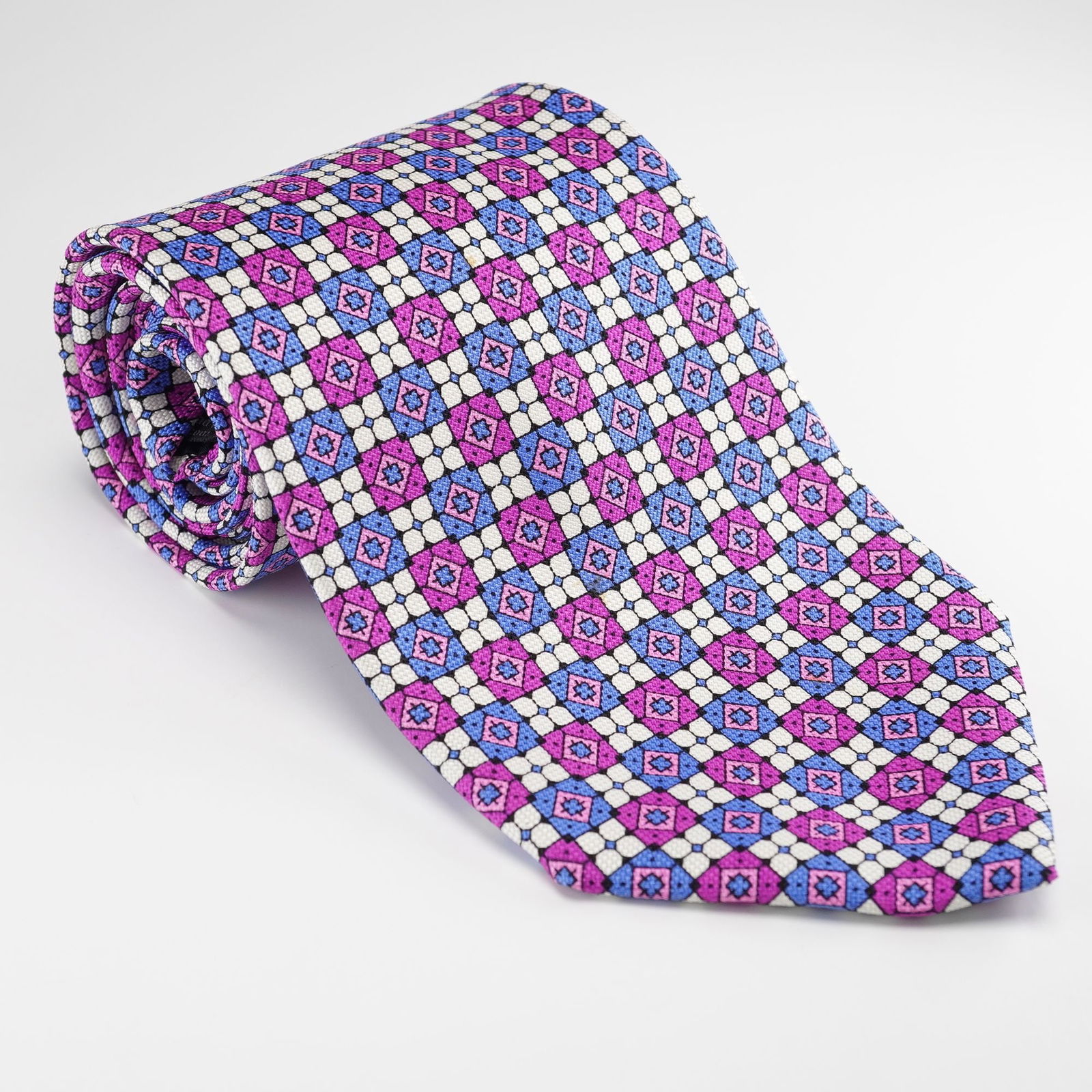 A Gianni Versace Magenta, Blue and White Geometric Silk Necktie: A Gianni Versace necktie crafted from 100% silk, featuring a repeating geometric pattern of interlocking squares and diamond shapes in shades of magenta, blue, and white. The reverse includes a woven