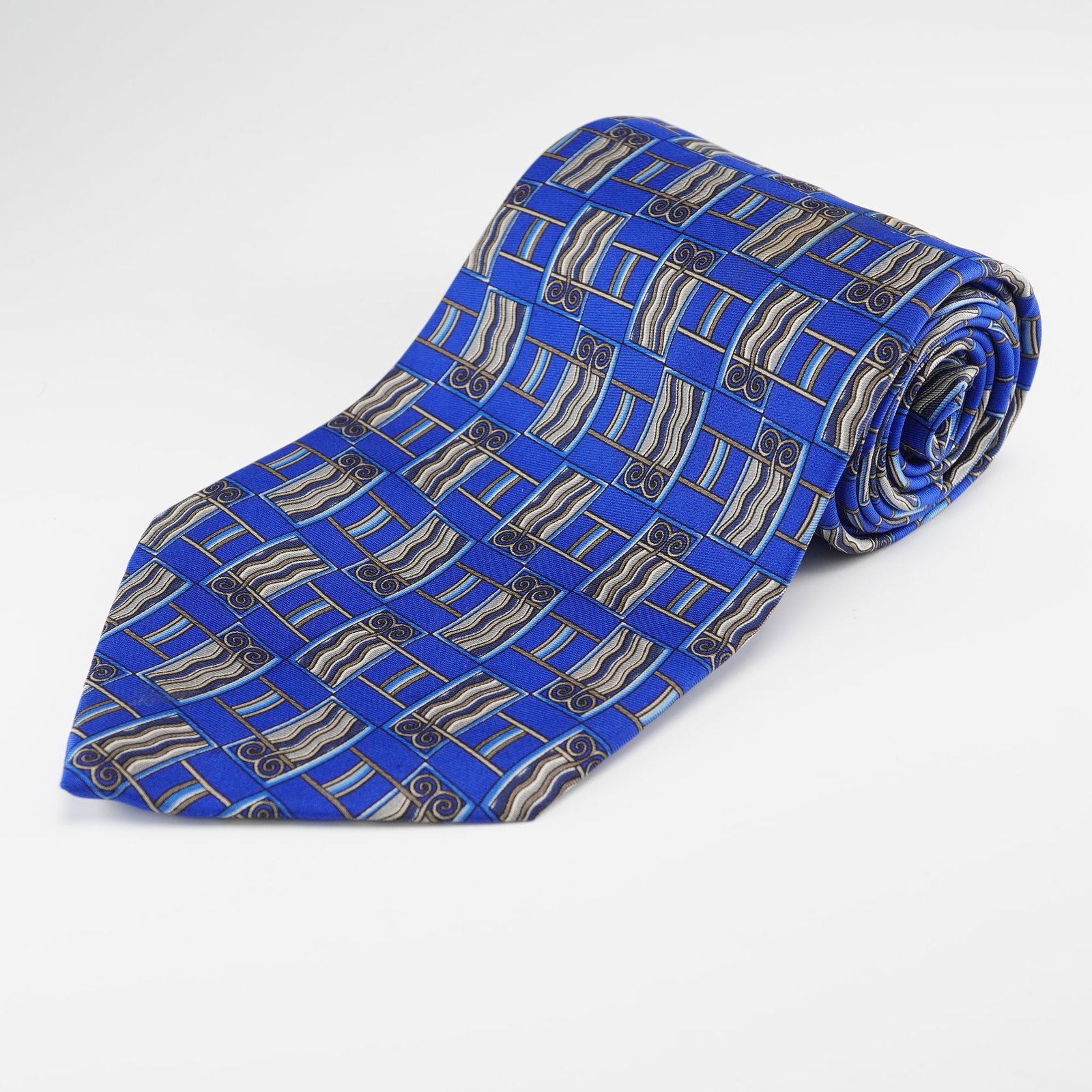 VALENTINO Mens Silk Geometric Pattern Necktie, Made in Italy: A Valentino mens necktie, crafted from 100% silk. The tie features a vibrant blue ground adorned with a repeating geometric pattern composed of rectangular blocks containing wavy lines and scroll moti