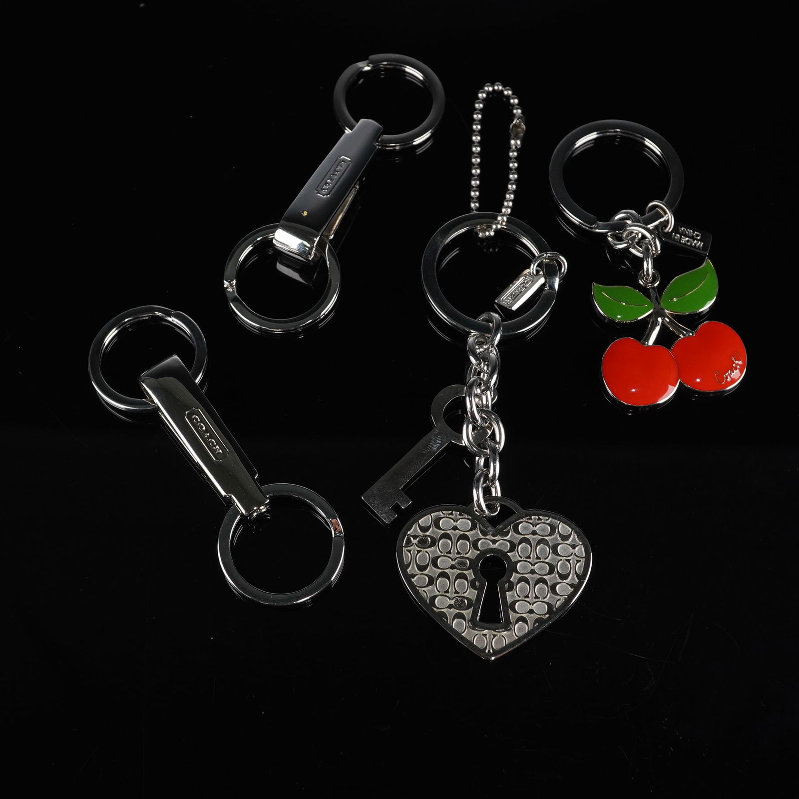 A Group of 4 Modern COACH Silver-Tone Keychains/Key Fobs: A group of four modern COACH keychains or key fobs, primarily constructed from polished silver-tone metal. The collection includes two keychains featuring rectangular clips embossed 'COACH' and attach