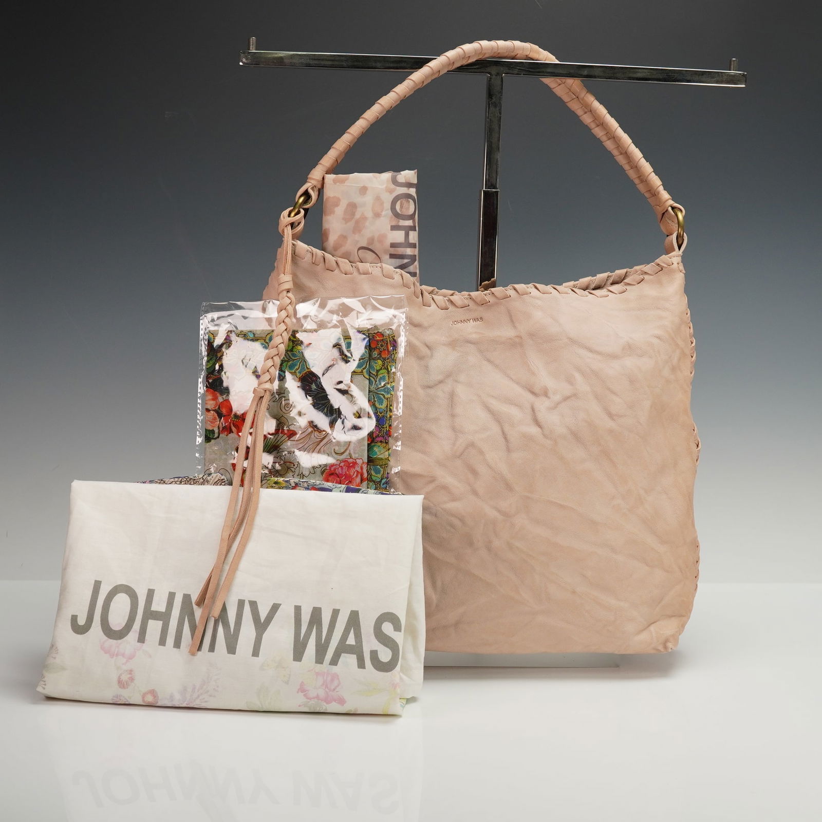 A Johnny Was Leather Shoulder Bag with Accompanying Accessories: The bag is made from soft, light beige-to-nude colored pebbled leather, featuring braided leather handles and decorative woven leather details on the sides. The brand name JOHNNY WAS is debossed into