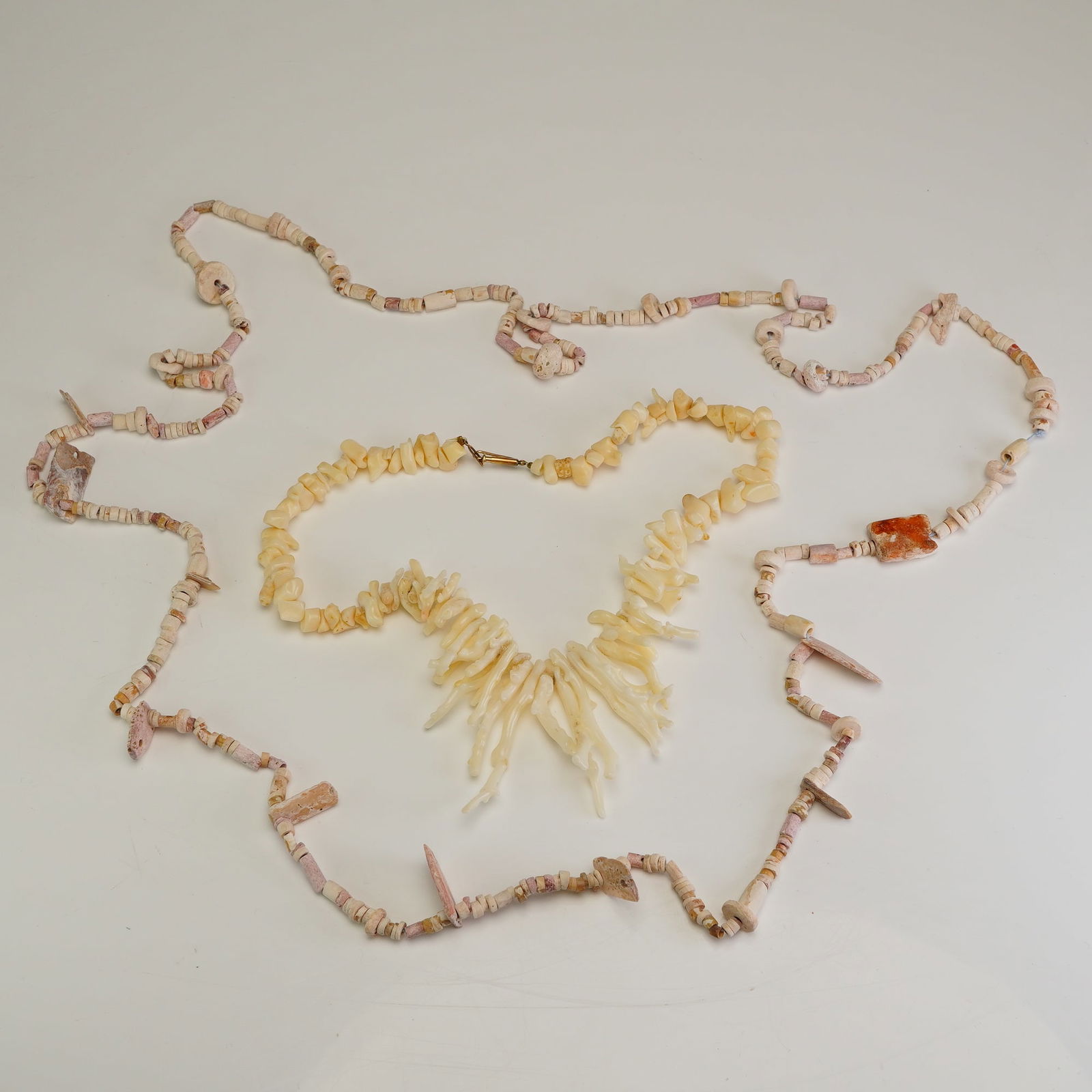 2pc Shell and Angel Skin Coral Bead Necklaces: This lot features two necklaces composed of natural organic materials. The first is a fringe-style necklace featuring graduated, polished angel skin white branch coral elements suspended from a strand