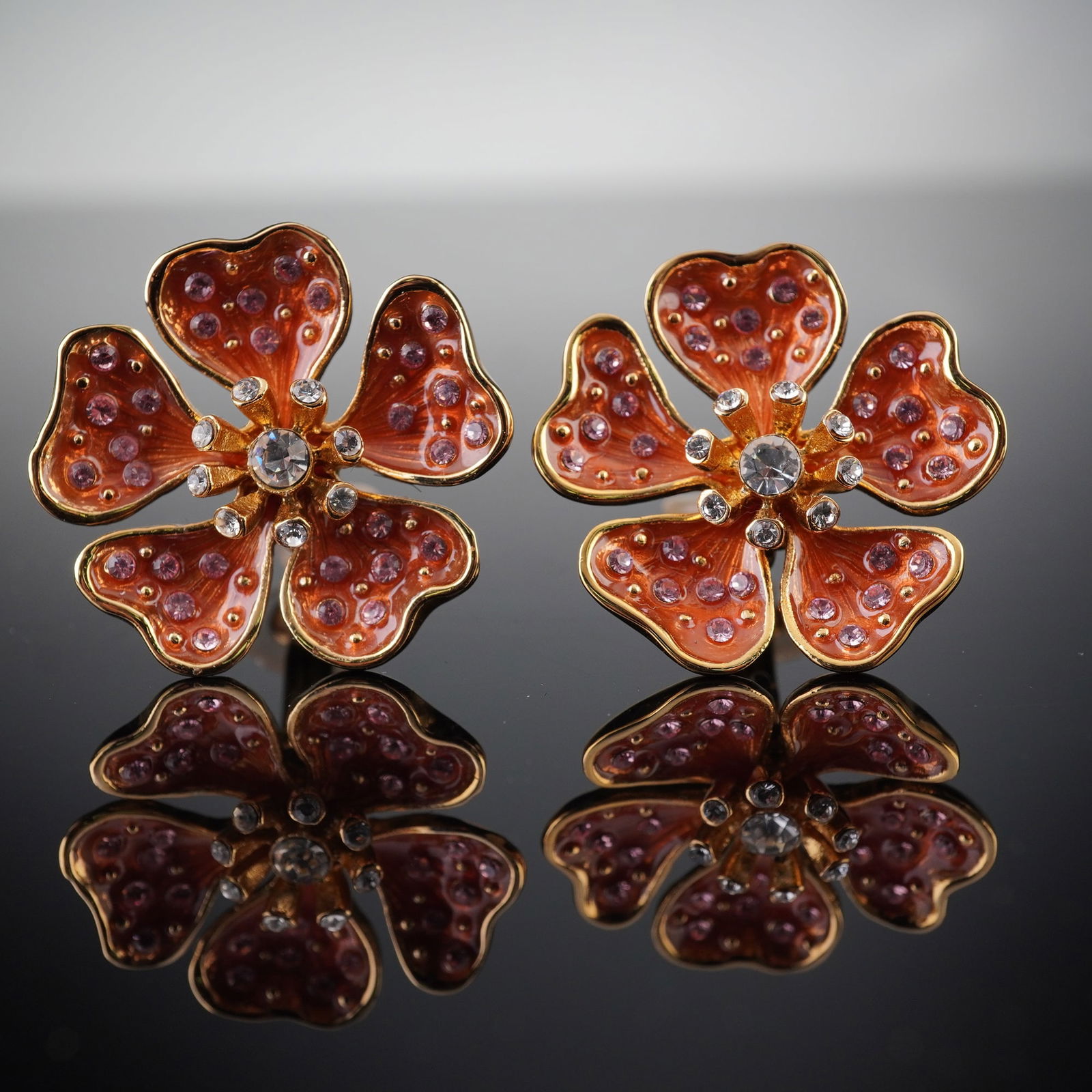 Gold-Tone Enamel & Rhinestone Floral Clip-On Earrings: A pair of gold-tone metal clip-on earrings, fashioned into a four-petal floral design. Each earring features a surface coated in vibrant orange-red enamel, studded with numerous small pink/purple rhin
