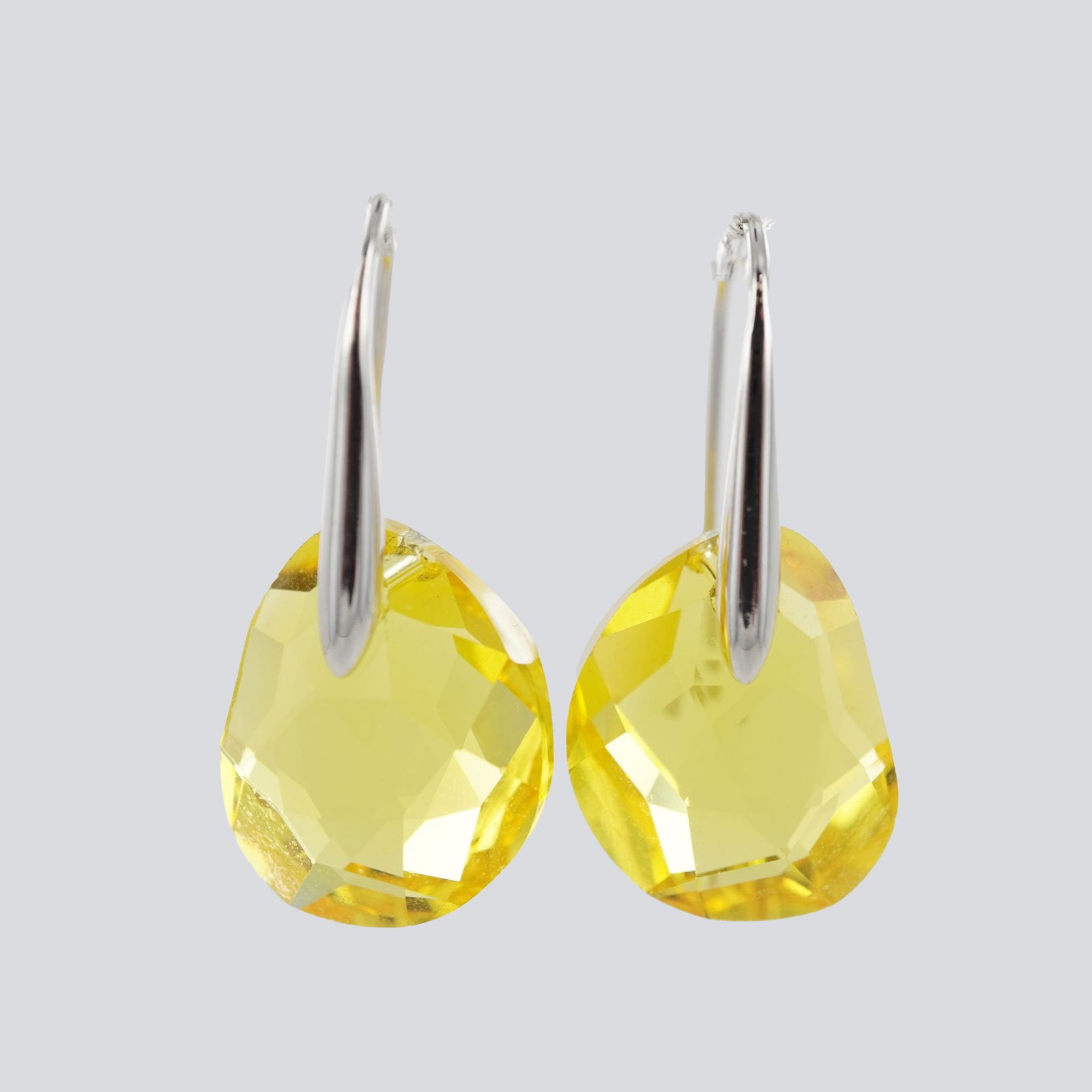 Pair of Silver-Tone Swarovski Yellow Faceted Crystal Drop Earrings: A pair of Swarovski drop earrings featuring faceted yellow quartz crystals, each etched with the Swarovski swan hallmark visible within the stone. The quartz drops are suspended from polished silver-t
