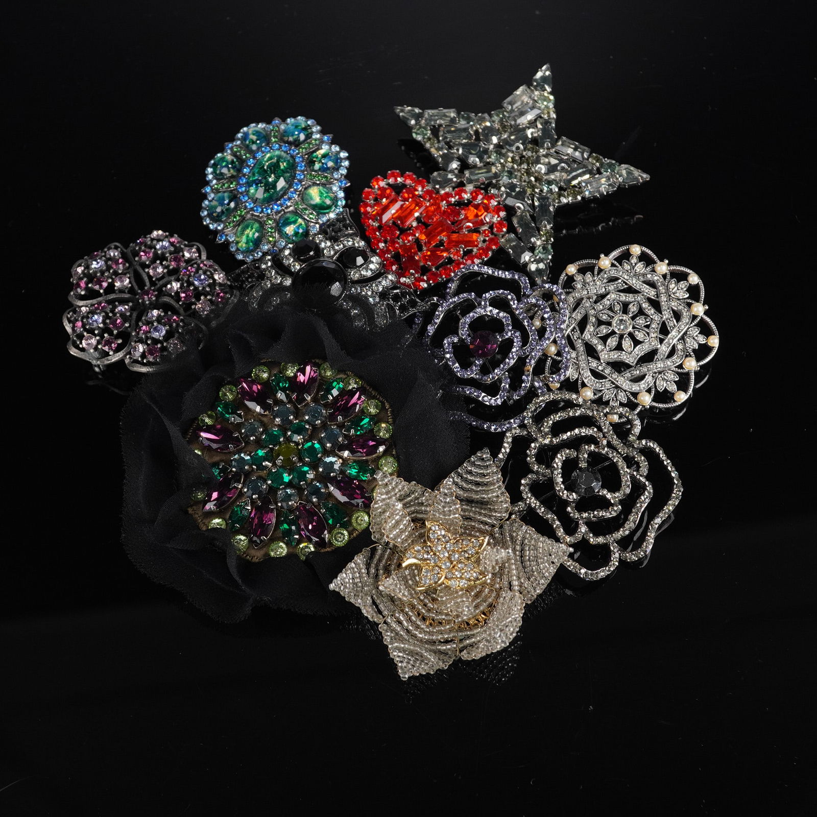 A Collection of Nine Rhinestone and Imitation Pearl Costume Jewelry: A collection of nine costume jewelry brooches, featuring diverse styles including floral, star, heart, abstract, and geometric motifs. They are primarily constructed from silver-tone and some gold-ton