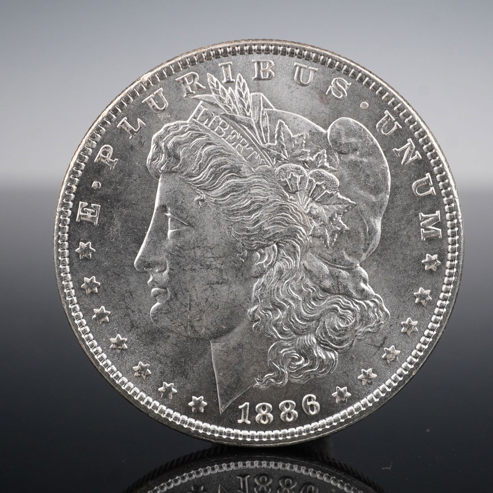 1886 Morgan Silver Dollar: Struck in 1886, this Morgan Silver Dollar is composed of 90% silver and 10% copper. The obverse presents George T. Morgan's neoclassical depiction of Liberty, wearing a Phrygian cap adorned with