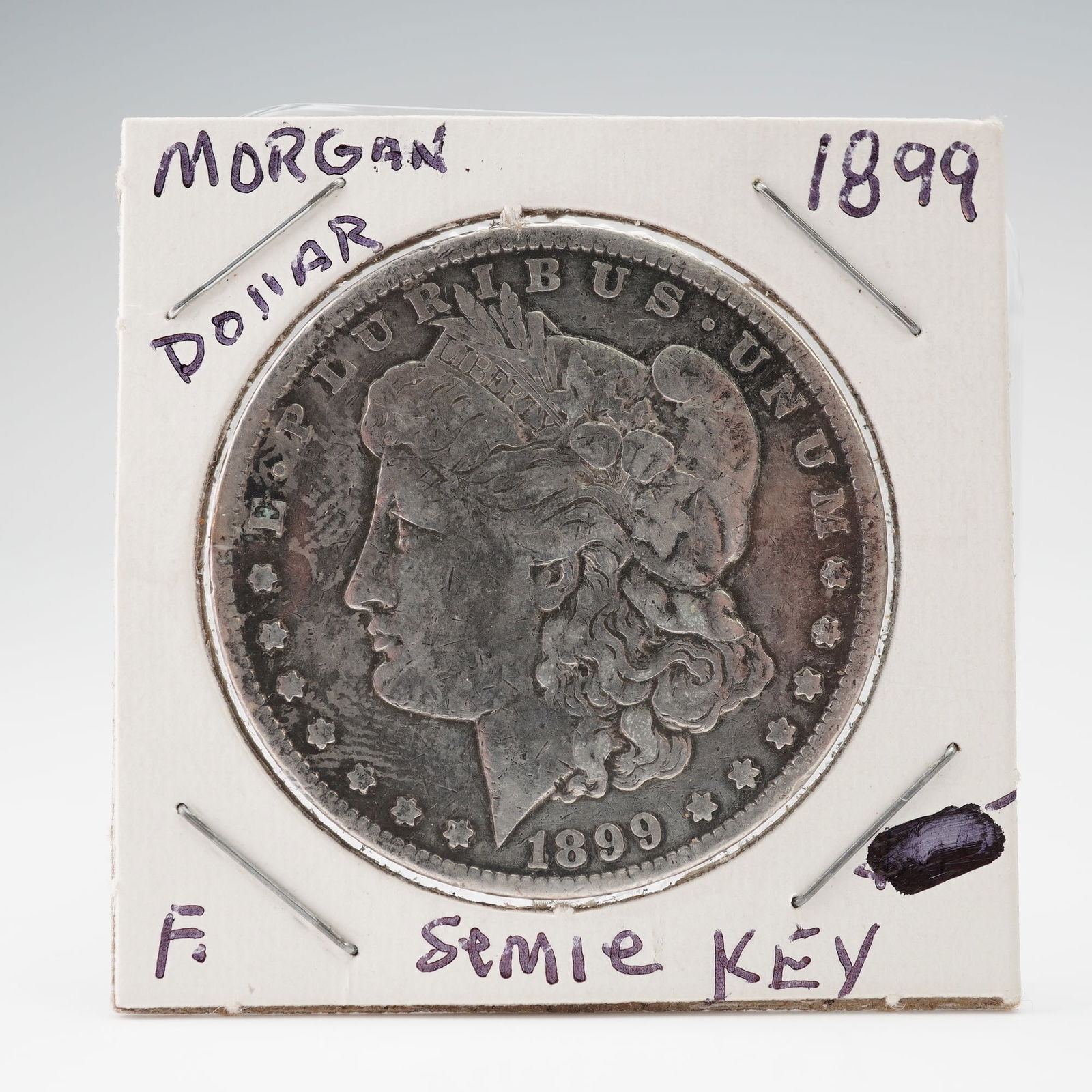 1899 Morgan Silver Dollar: A coin with it's obverse features a left-facing portrait of Liberty wearing a Phrygian cap adorned with wheat and cotton, symbolizing agricultural prosperity, surrounded by the inscription E PLURIBUS