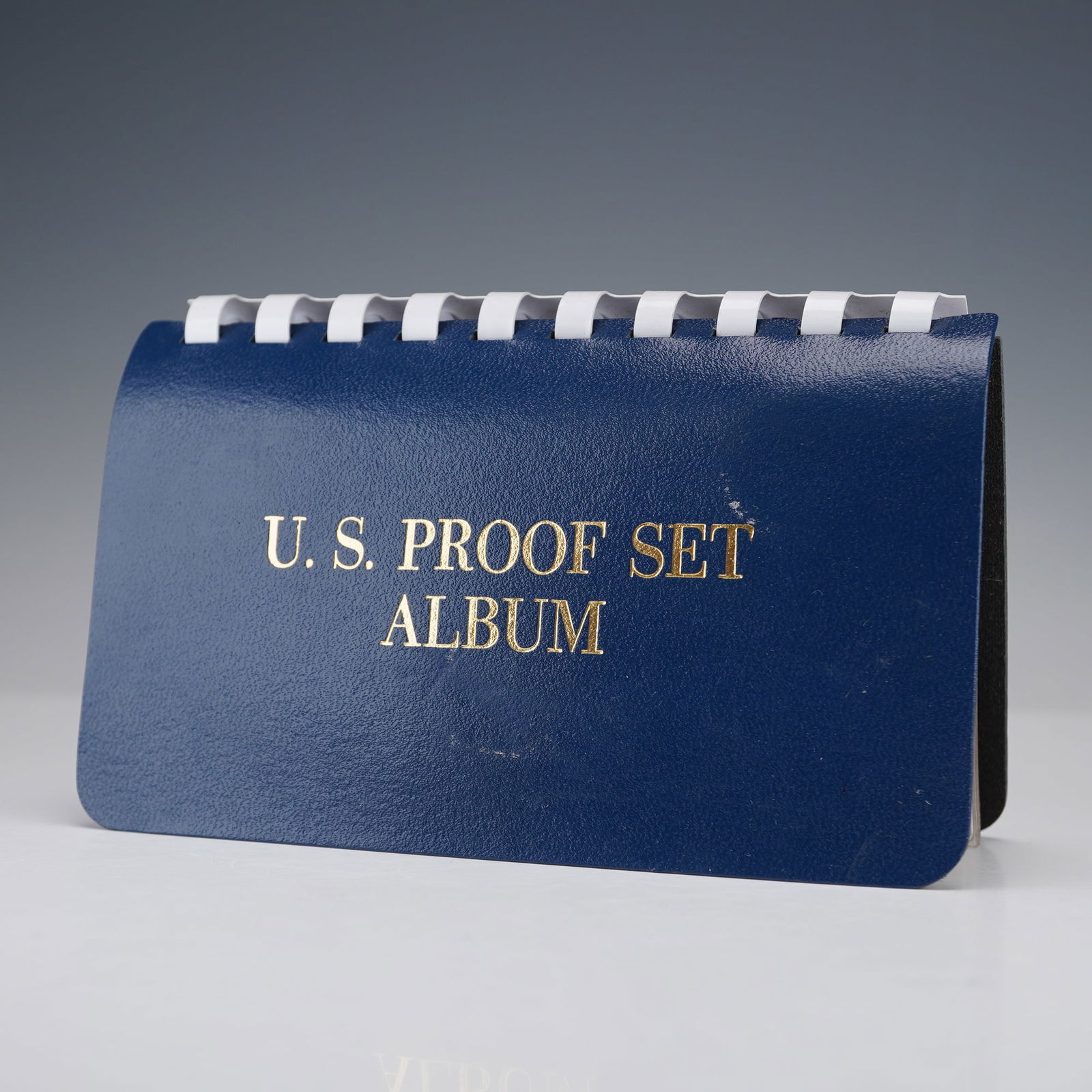 1956 - 1963 U.S. Mint 5-Coin Proof Set Album - 8 Pages: A collection of eight consecutive U.S. Mint proof sets housed in a blue spiral-bound U.S. Proof Set Album with gold-stamped cover lettering. This grouping includes proof coins from years 1956 through