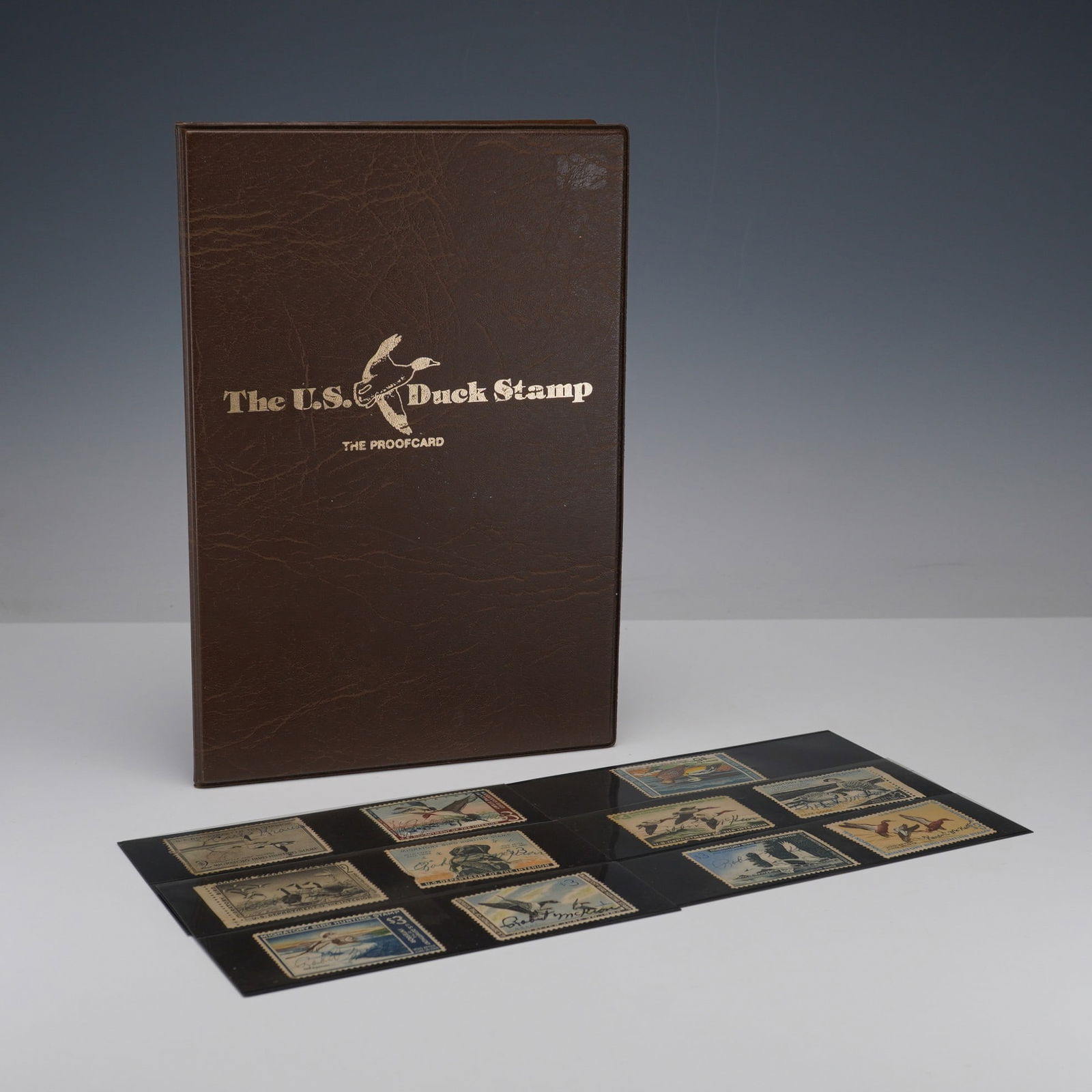 5pc U.S. Duck Stamp Proofcard Album and Federal Duck Stamps: Presented in a brown leatherette folder titled The U.S. Duck Stamp The Proofcard, this set includes the 1985 and 1986 Federal Duck Stamp First Day of Issue displays, each mounted with the original sta