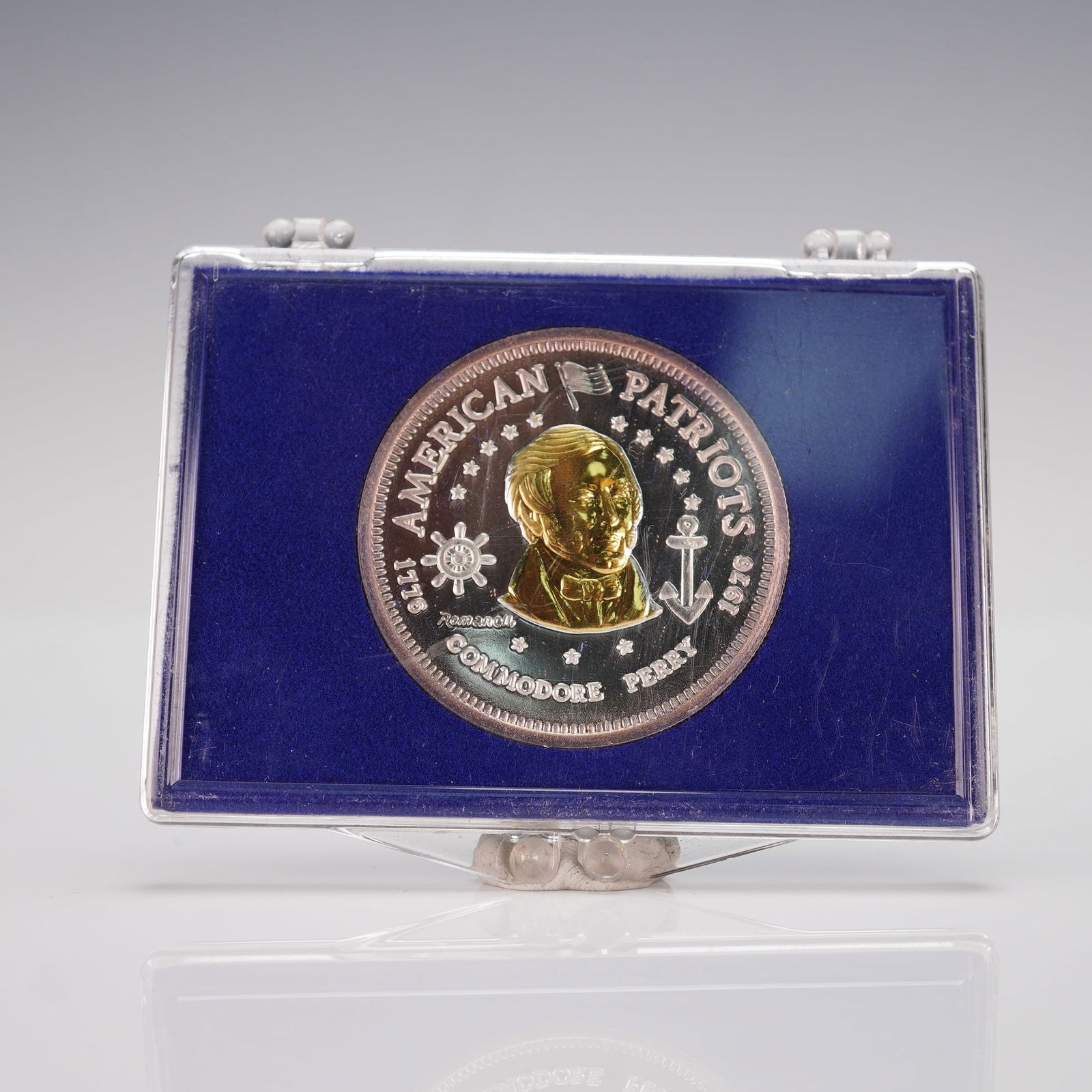 1976-L Commodore Perry American Patriots Silver and Gold Bullion: A dual-metallic design with a silver planchet and gold-plated portrait. The obverse presents a central bust of Commodore Perry surrounded by nautical emblems, stars, and the inscriptions AMERICAN PATR