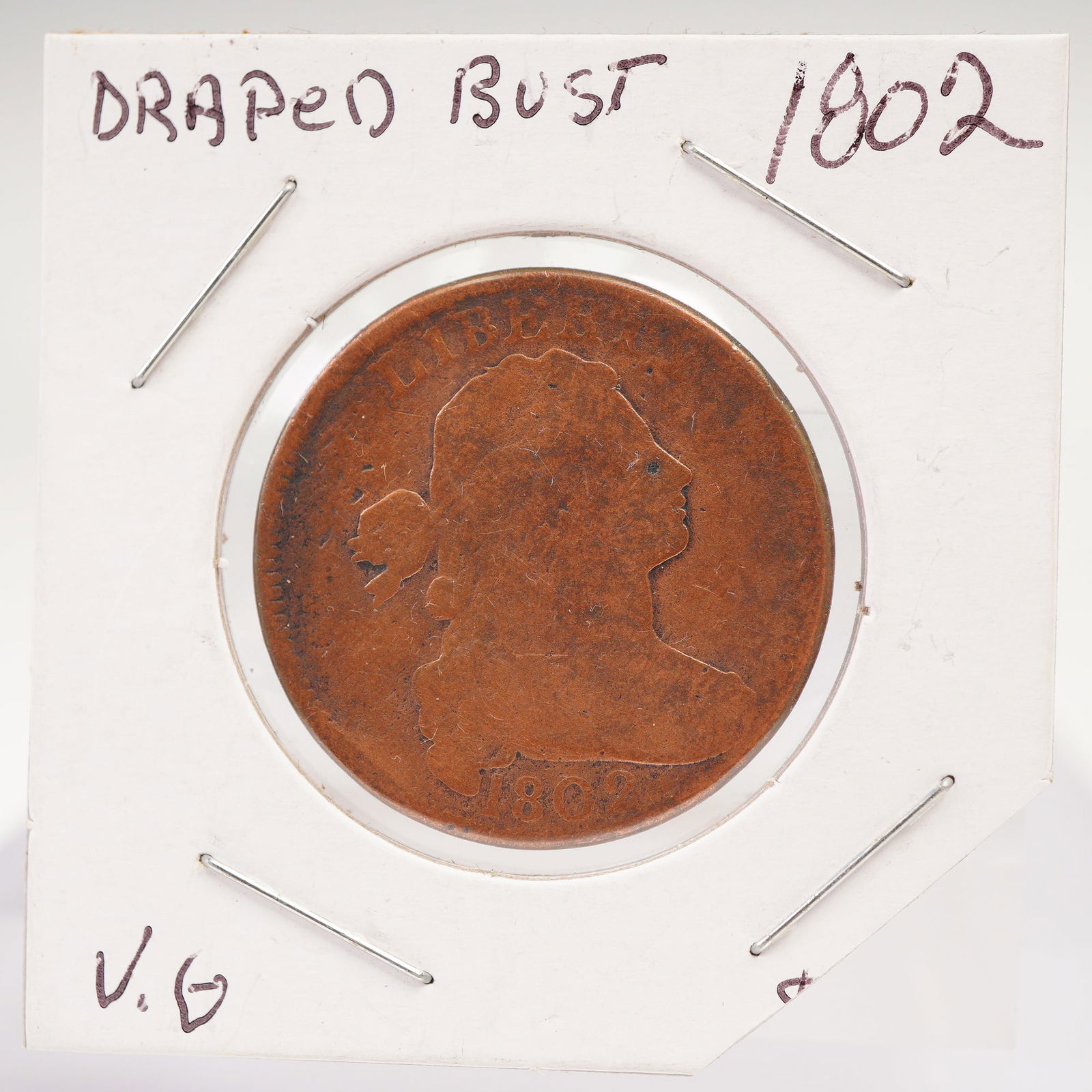 1802 United States Draped Bust One Cent Coin: Composed of copper, the obverse presents the Draped Bust with Liberty depicted in right-facing profile surrounded by LIBERTY above and the year below. The reverse formed by a wreath tied with a ribbon