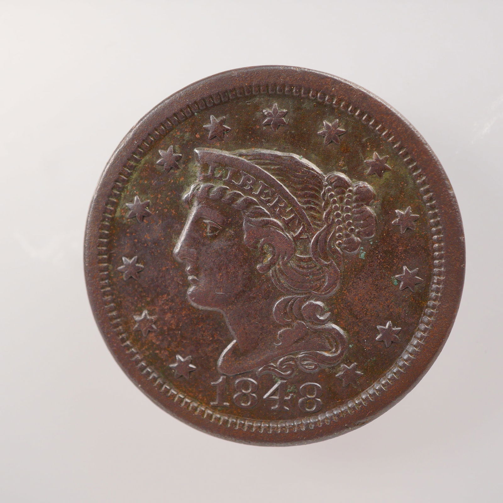 1848 Liberty Braided Hair One Cent Coin: The obverse portrait of Liberty wearing a coronet inscribed with her name, encircled by thirteen stars, and the year below. The reverse bears a wreath surrounding the denomination ONE CENT. Composed o