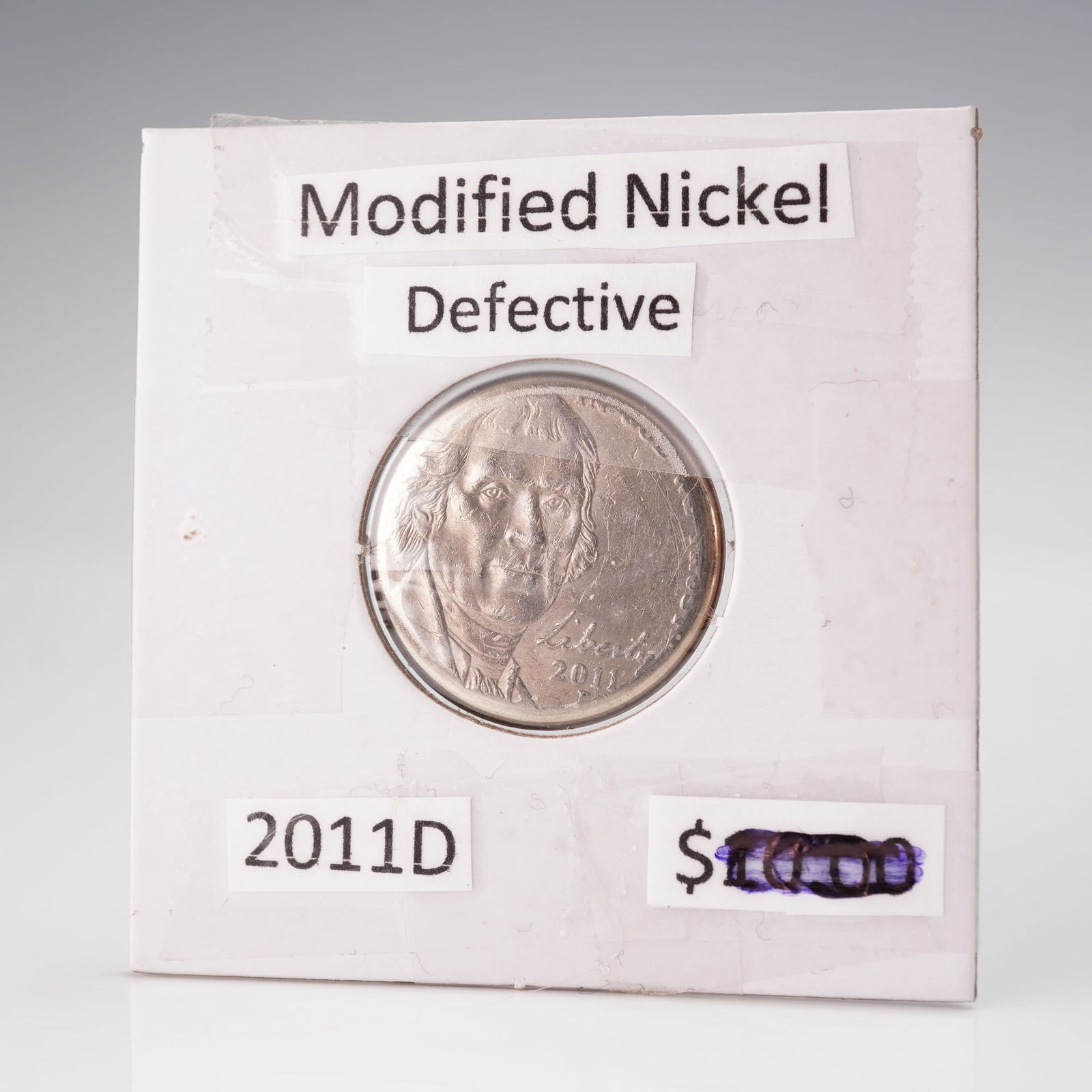 2011 P United States Jefferson Nickel, Modified and Defective: A United States Jefferson Nickel, dated 2011 with a P mint mark, presented in a standard white cardboard coin holder featuring a clear plastic window. The obverse displays a portrait of Thomas Jeffers