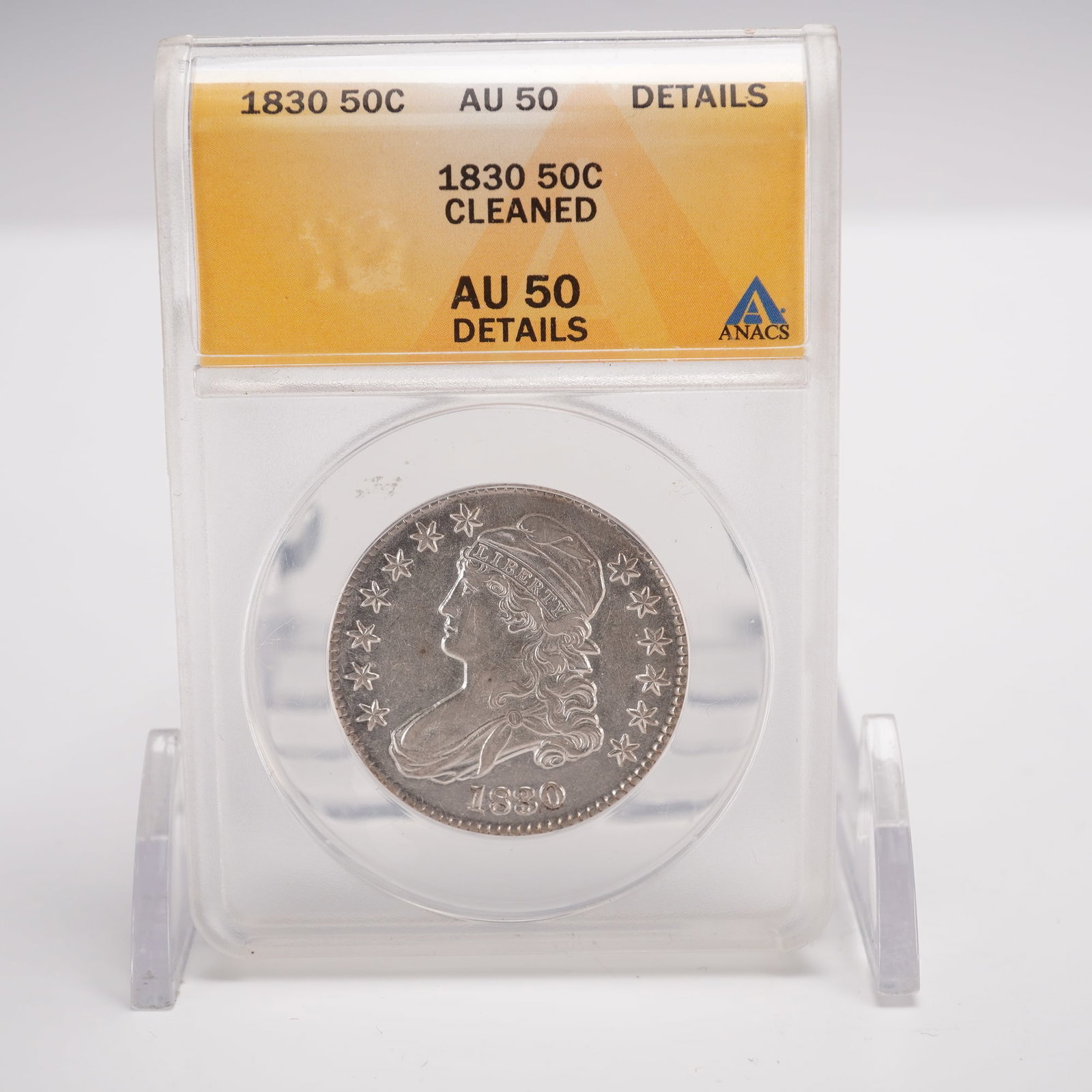 1830 Capped Bust Half Dollar ANACS Graded AU 50 Cleaned: The obverse features the bust of Liberty facing left, adorned with a Phrygian or Freedom Cap, a symbol associated with the Revolutionary era. Her flowing hair cascades down, with a portion of her gown