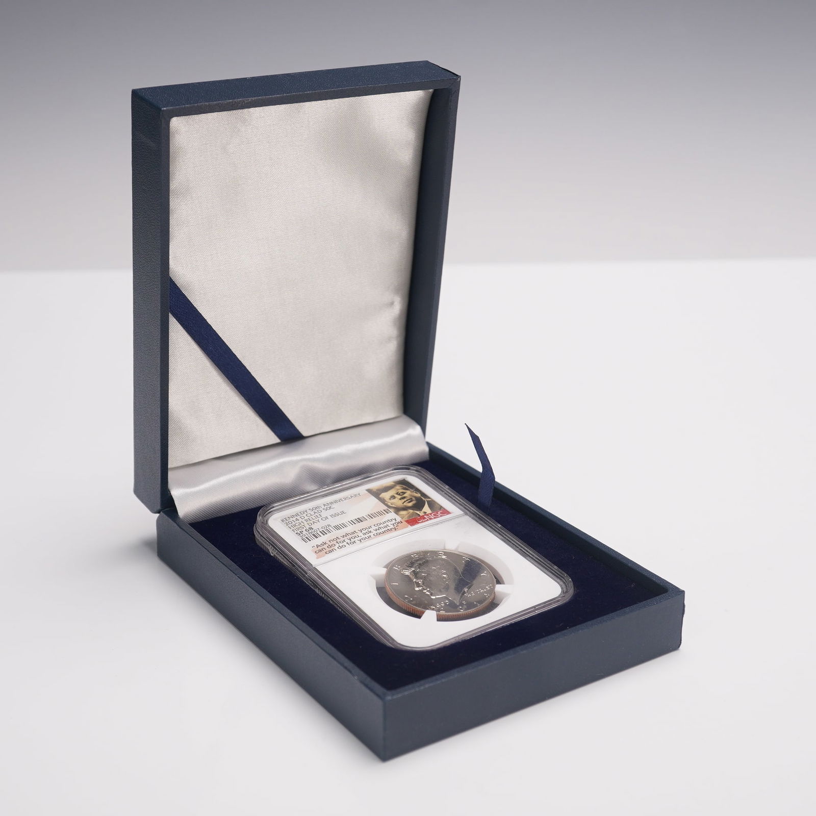 2014-D Kennedy 50th Anniversary Clad Half Dollar NGC Graded SP 68 FDOI: Kennedy 50th Anniversary Clad Half Dollar, graded SP 68 by NGC and designated First Day of Issue. Struck at the Denver Mint, this high relief coin is encapsulated in a protective NGC holder. The obver