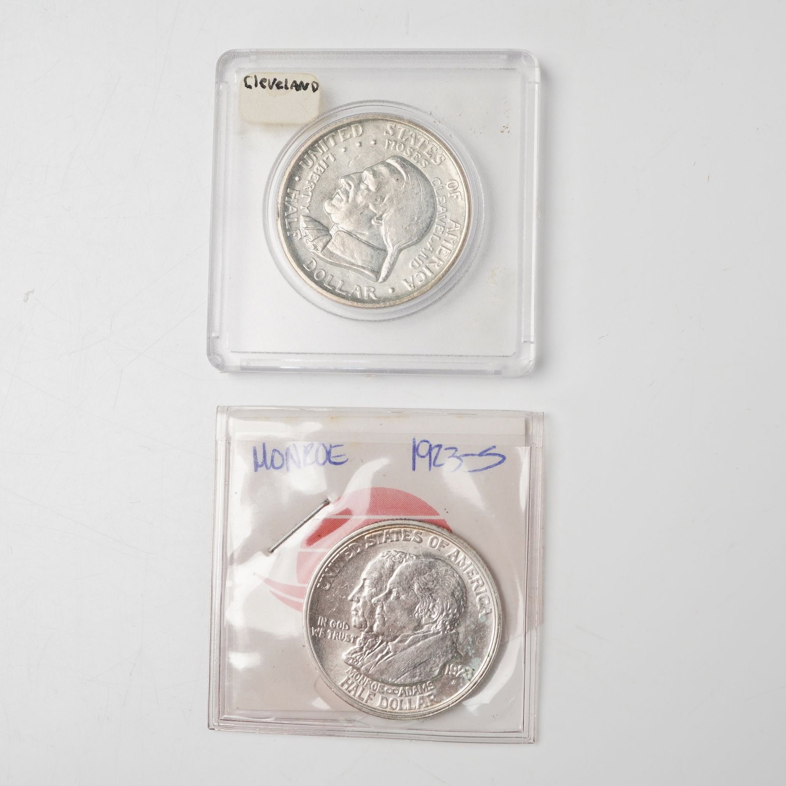 2pc 1923-S & 1936 United States Commemorative Half Dollar Coins: Features a 1936 Cleveland Great Lakes Exposition half dollar depicting the profile of Moses Cleveland and an allegorical map of the Great Lakes punctuated by stars, paired with a 1923-S Monroe Doctrin